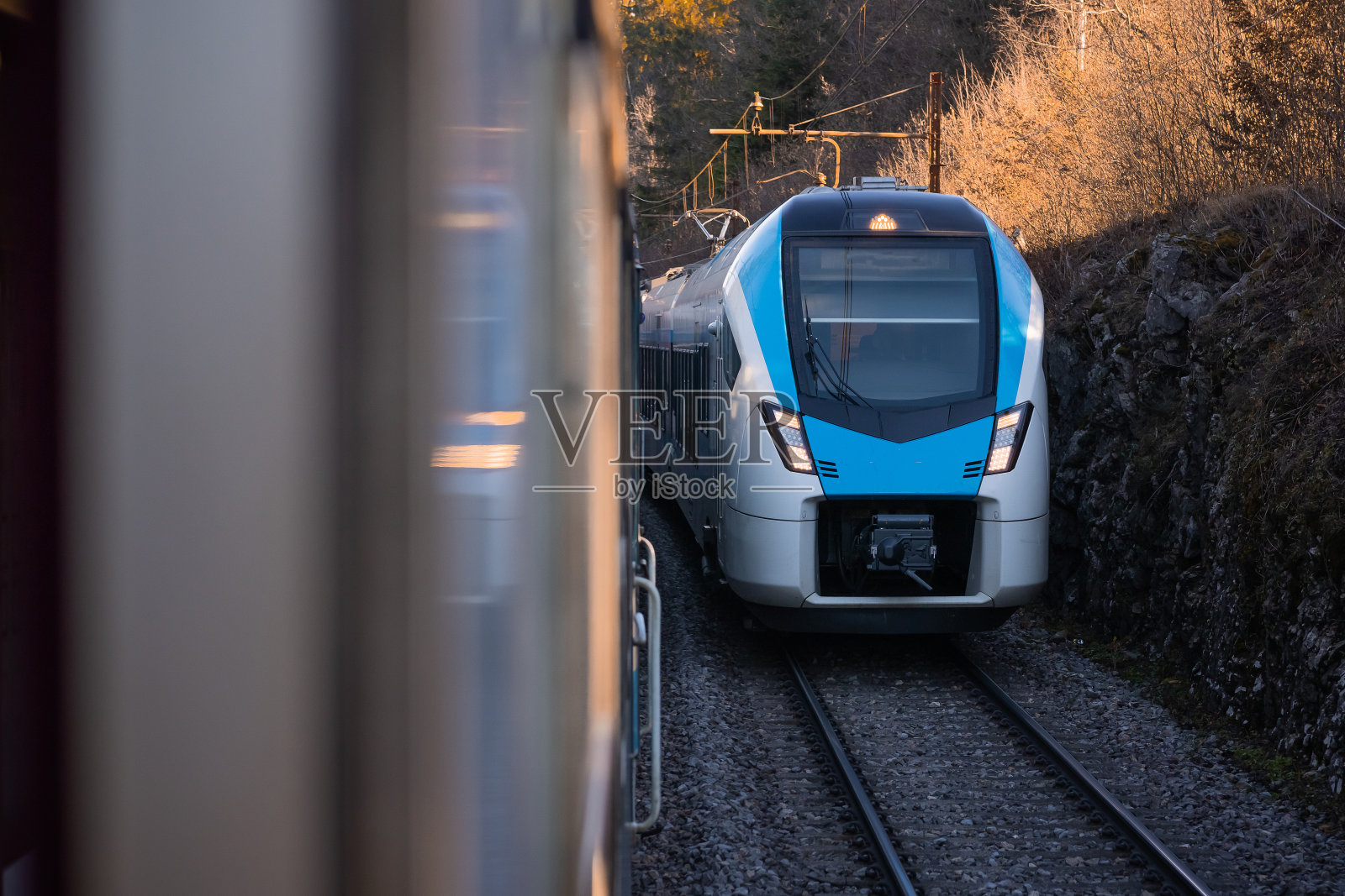 现代的蓝白相间的客运列车正驶向相邻轨道上的另一列列车。两列火车在平行的轨道上相遇。照片摄影图片