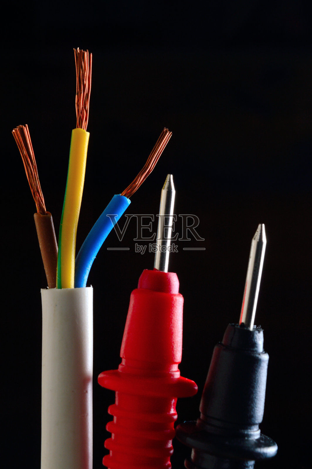 剥离，三芯导线和万用表探头在黑暗的背景。黑色背景的特写镜头。照片摄影图片