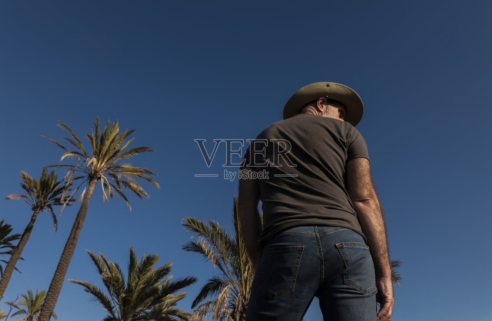 戴着牛仔帽的成年男子在塔伯纳斯沙漠，棕榈树映衬着蓝天。西班牙阿尔梅里亚照片摄影图片