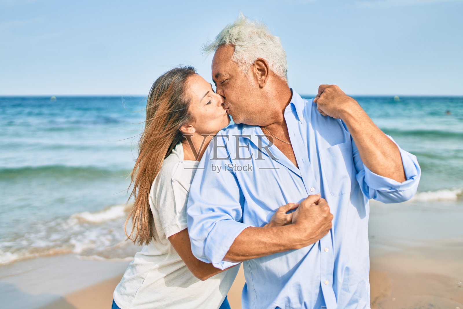 一对中年西班牙夫妇微笑着拥抱在海滩上散步照片摄影图片