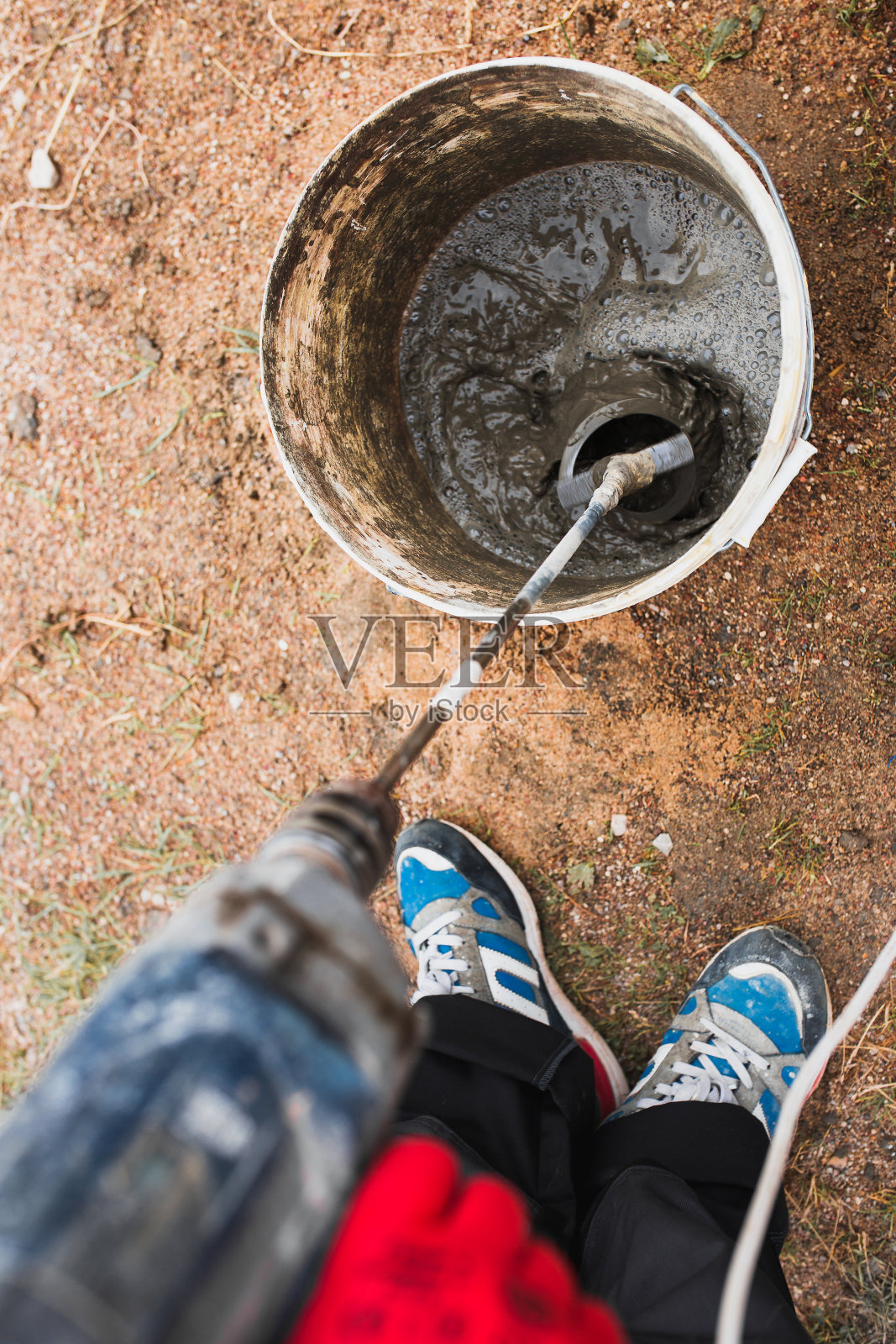 在一桶水泥和沙子中使用钻头上的搅拌机喷嘴配制水泥胶砂浆照片摄影图片