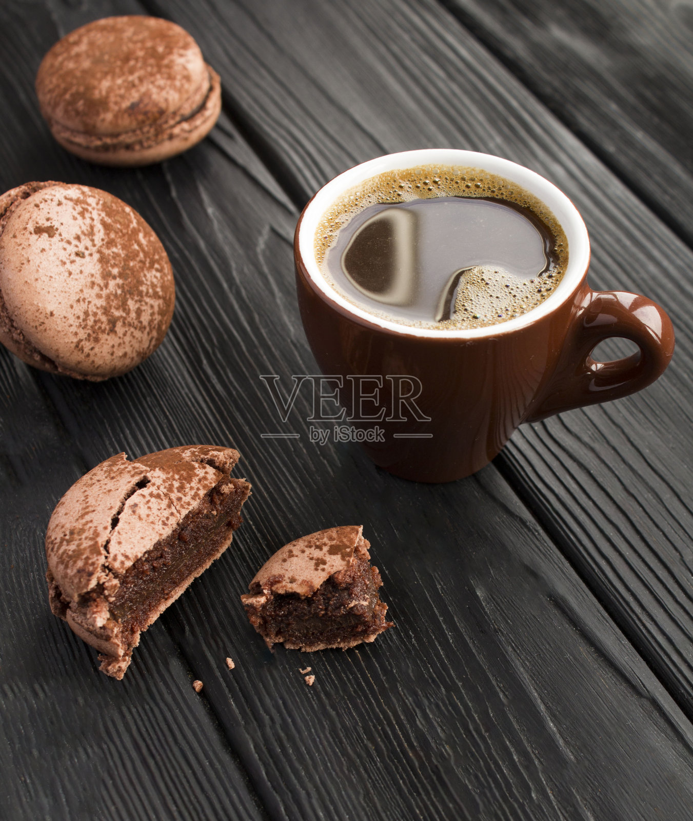 棕色陶瓷杯里的黑咖啡，黑色木质背景上的巧克力马卡龙照片摄影图片