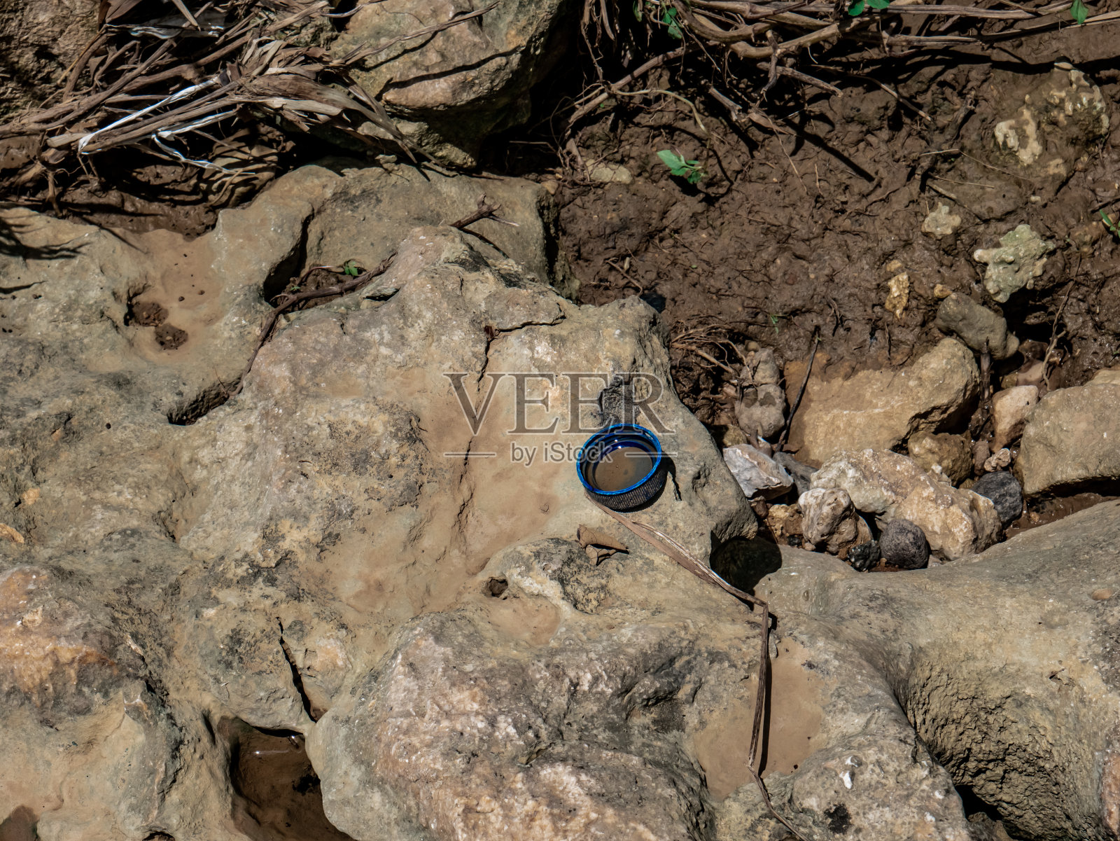 蓝色饮用水瓶的瓶盖在河边的岩石上照片摄影图片