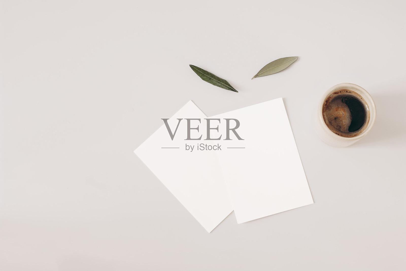空白贺卡和米色背景的橄榄树叶子。婚礼请柬模型场景。一杯咖啡。早餐的概念。平躺，顶视图。工作台及办公设备。照片摄影图片