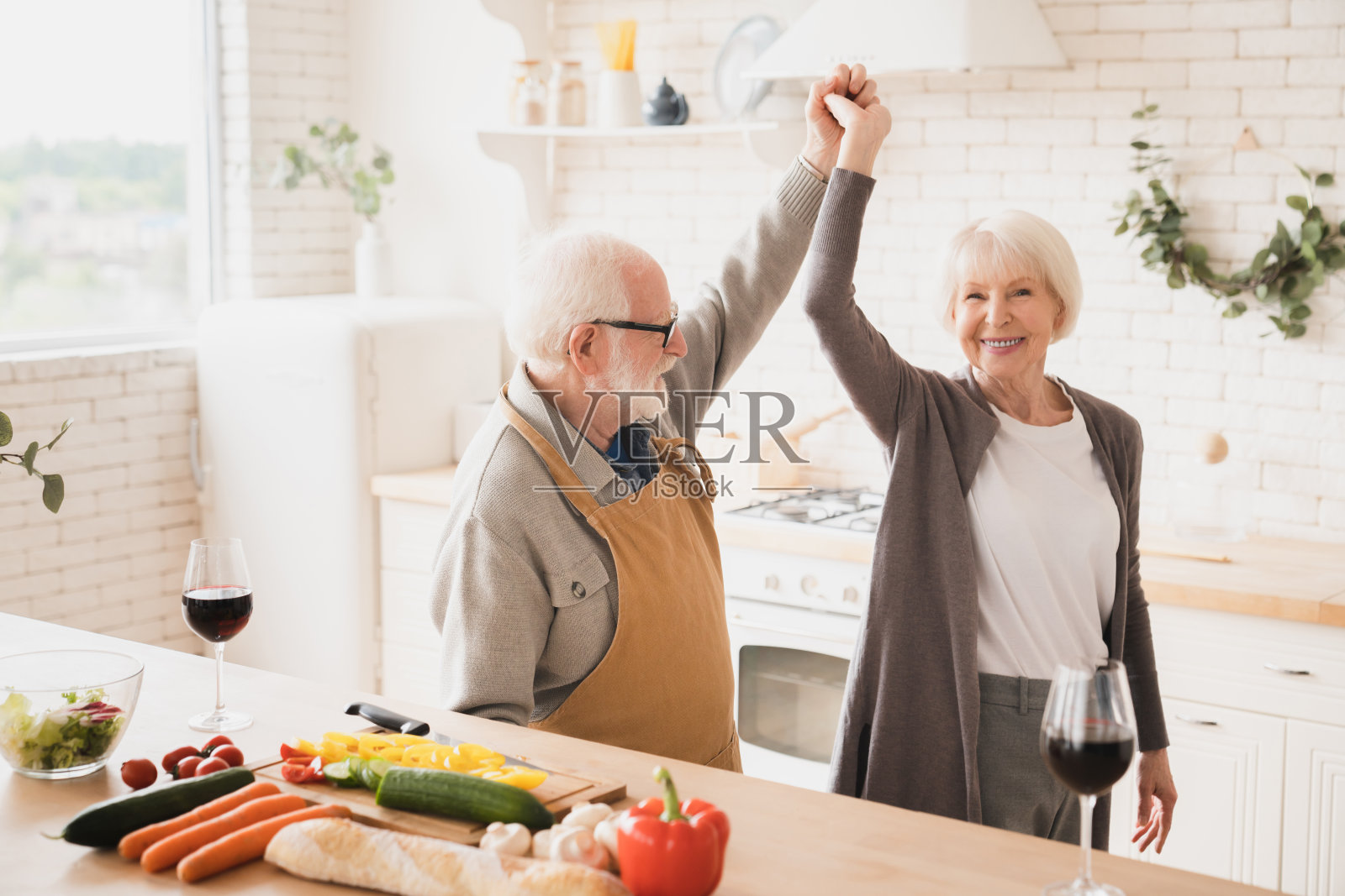 活跃的老年人。跳舞的老人，快乐的老人夫妇，配偶，祖父母花时间在一起，烹饪浪漫的晚餐，做沙拉。在家厨房健康饮食照片摄影图片