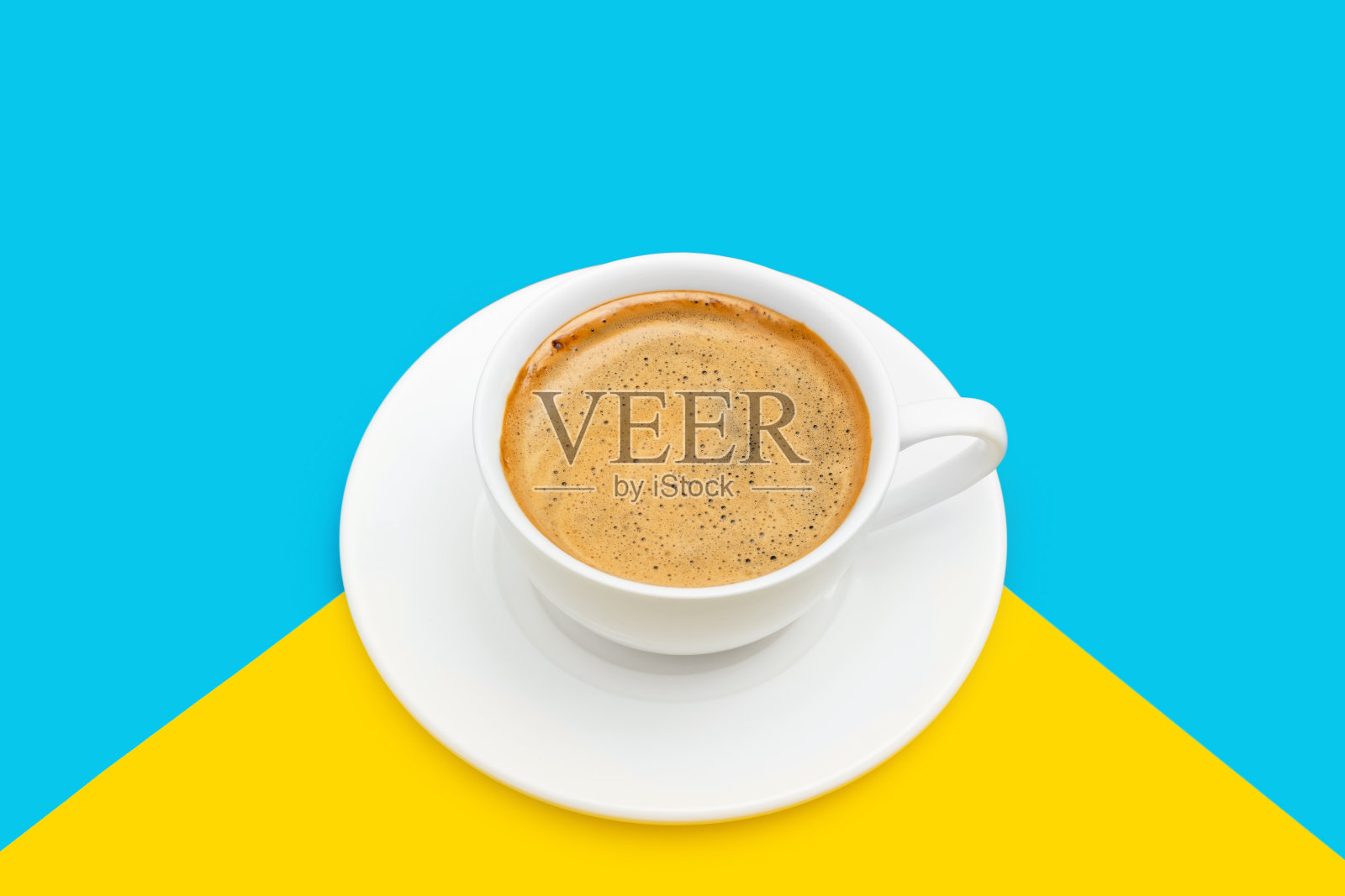 黑咖啡与泡沫在一个白色的杯盘，蓝色和黄色的背景照片摄影图片