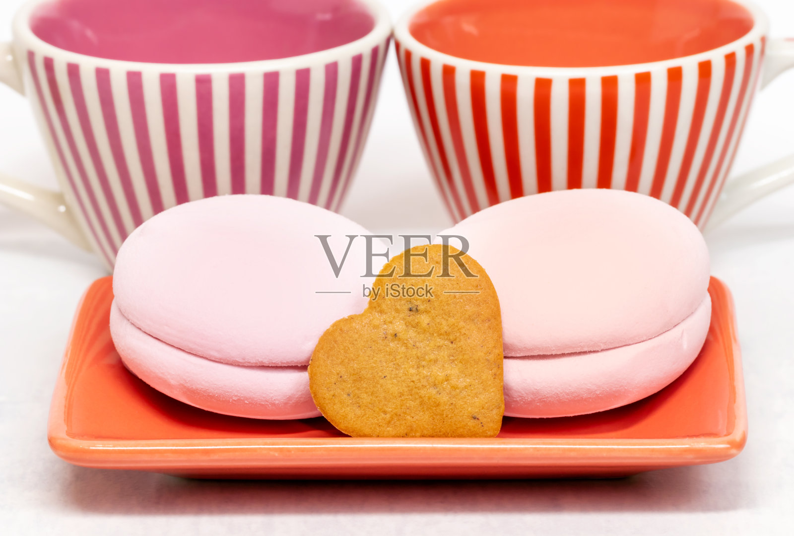 碟子上的甜棉花糖和两个陶瓷杯背景上的心形饼干。特写镜头。两人份的美味早餐。照片摄影图片