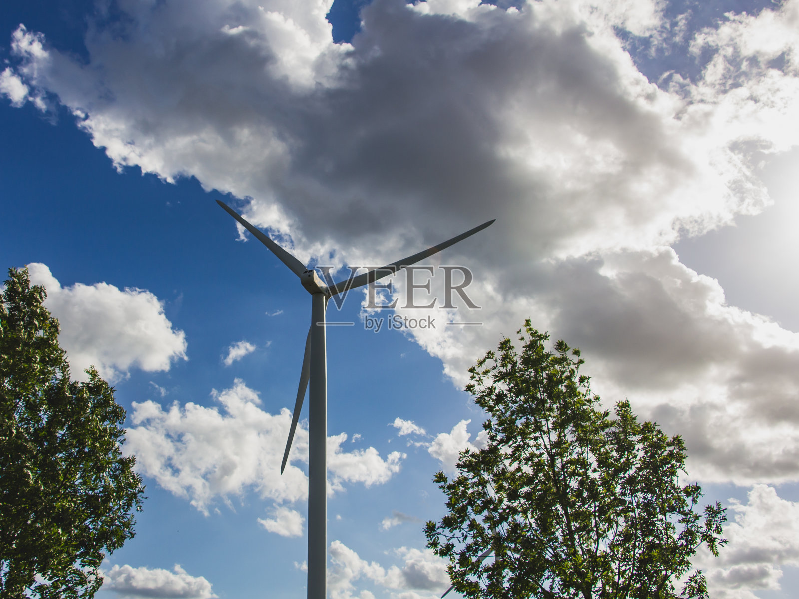 蓝色多云的天空和绿色的树木背景上的风力涡轮机照片摄影图片