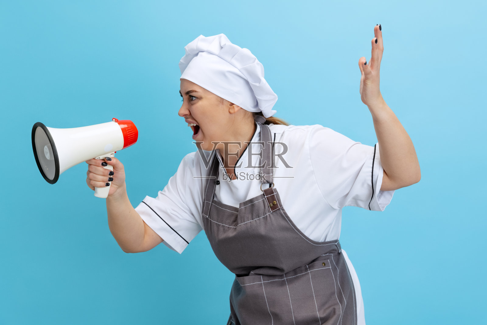 年轻女子的肖像，女厨师，厨师穿着白色制服，在蓝色背景下对着扩音器大喊大叫。烹饪、专业、经营、美食、口味、餐厅概念。照片摄影图片