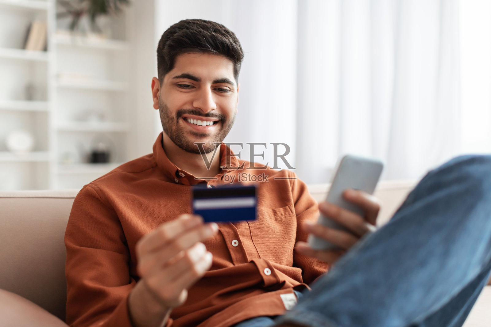 微笑的阿拉伯人在家里用手机和信用卡照片摄影图片