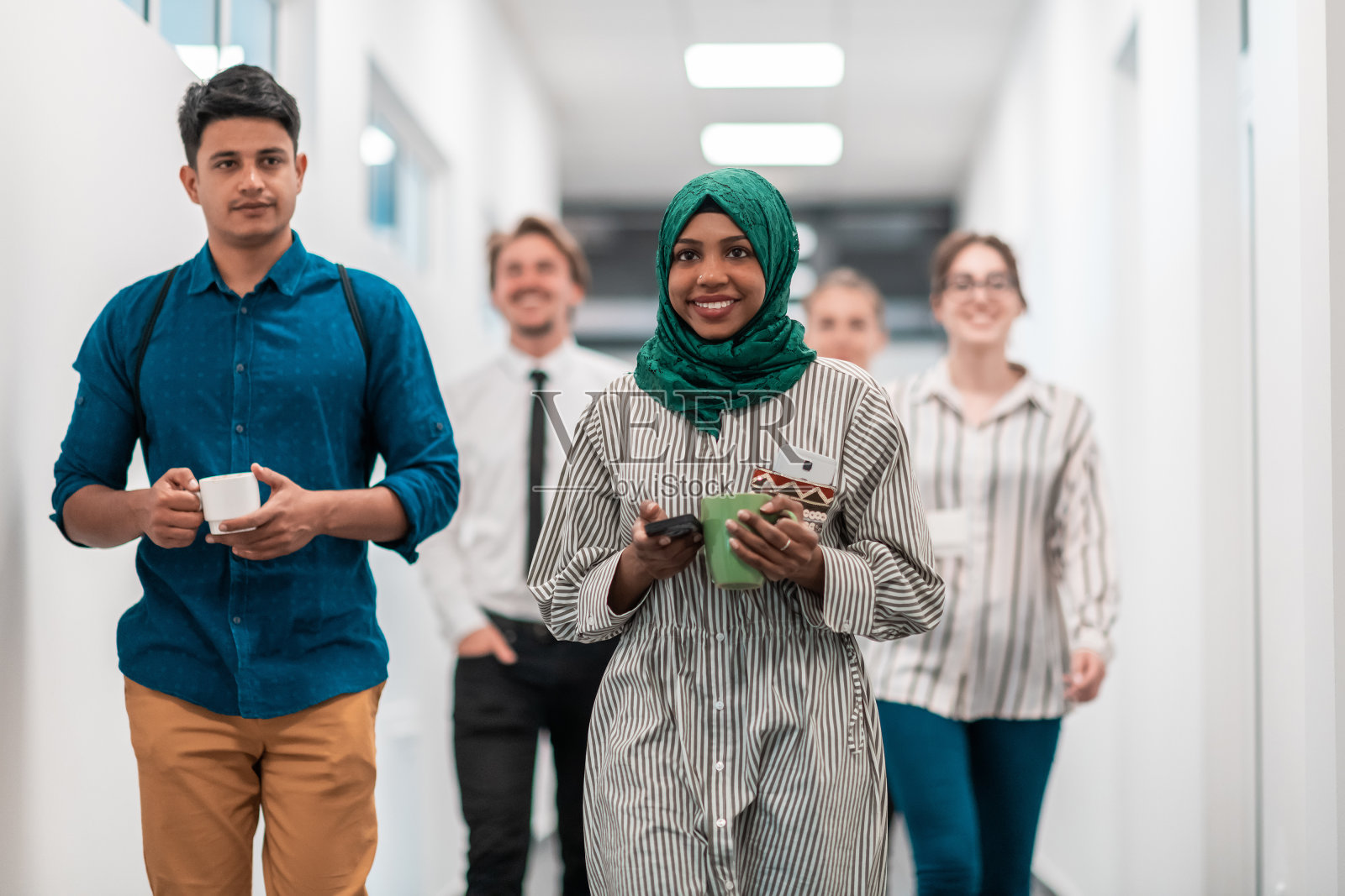 多种族创业团队在喝完咖啡休息回来时穿过大楼的走廊照片摄影图片