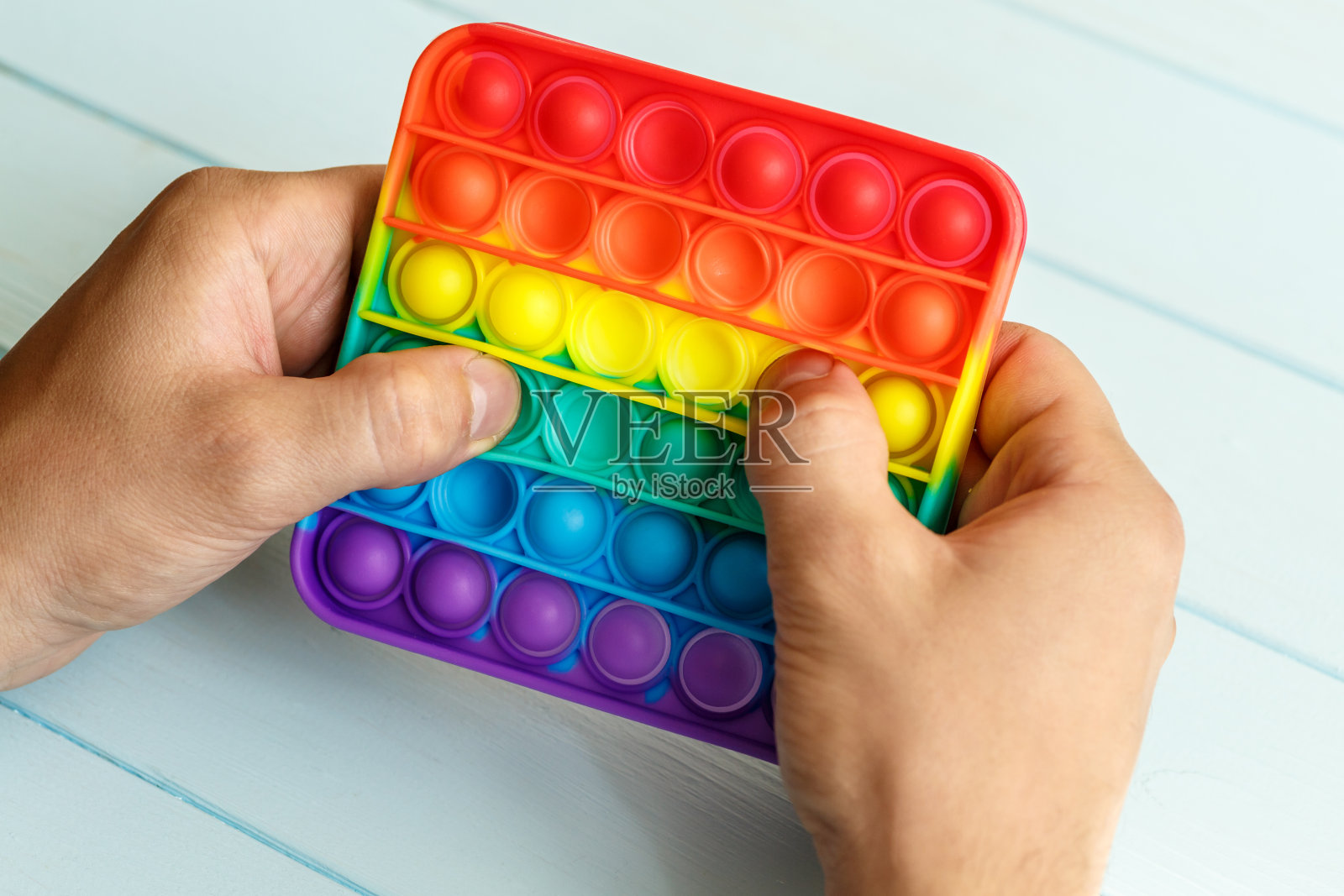 一个男人的手压在一个彩色彩虹硅胶抗压力玩具上，把它打开。放松多色感官pop它玩具。新型感官抗压力玩具，适合儿童和成人。照片摄影图片