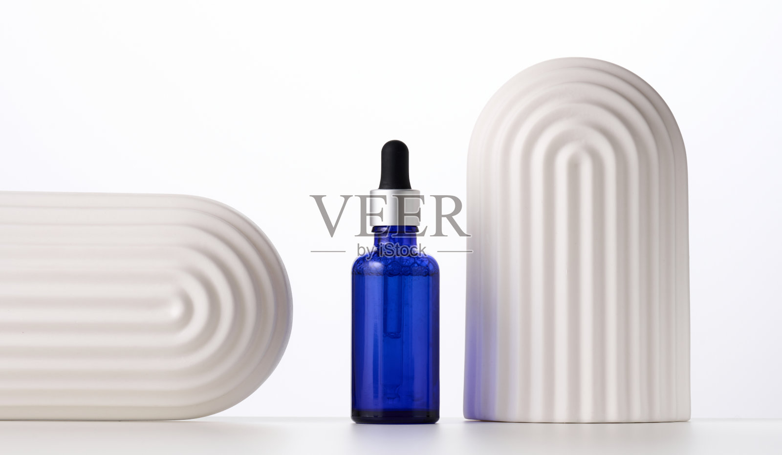蓝色玻璃瓶，带吸液器，白色背景上的白色装饰拱门。化妆品液体产品的模板，广告和促销照片摄影图片