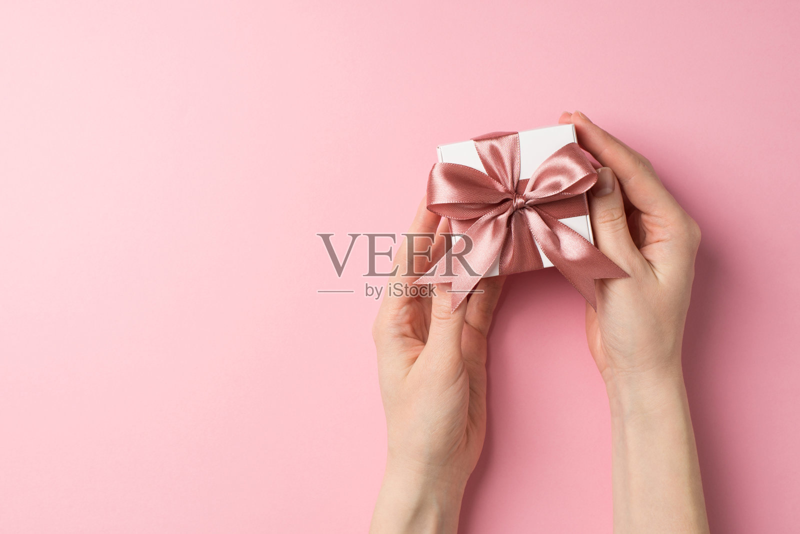 第一人称俯视图照片的情人节装饰女孩的手拿小白色礼品盒粉红色丝带蝴蝶结在孤立的淡粉色背景copyspace照片摄影图片