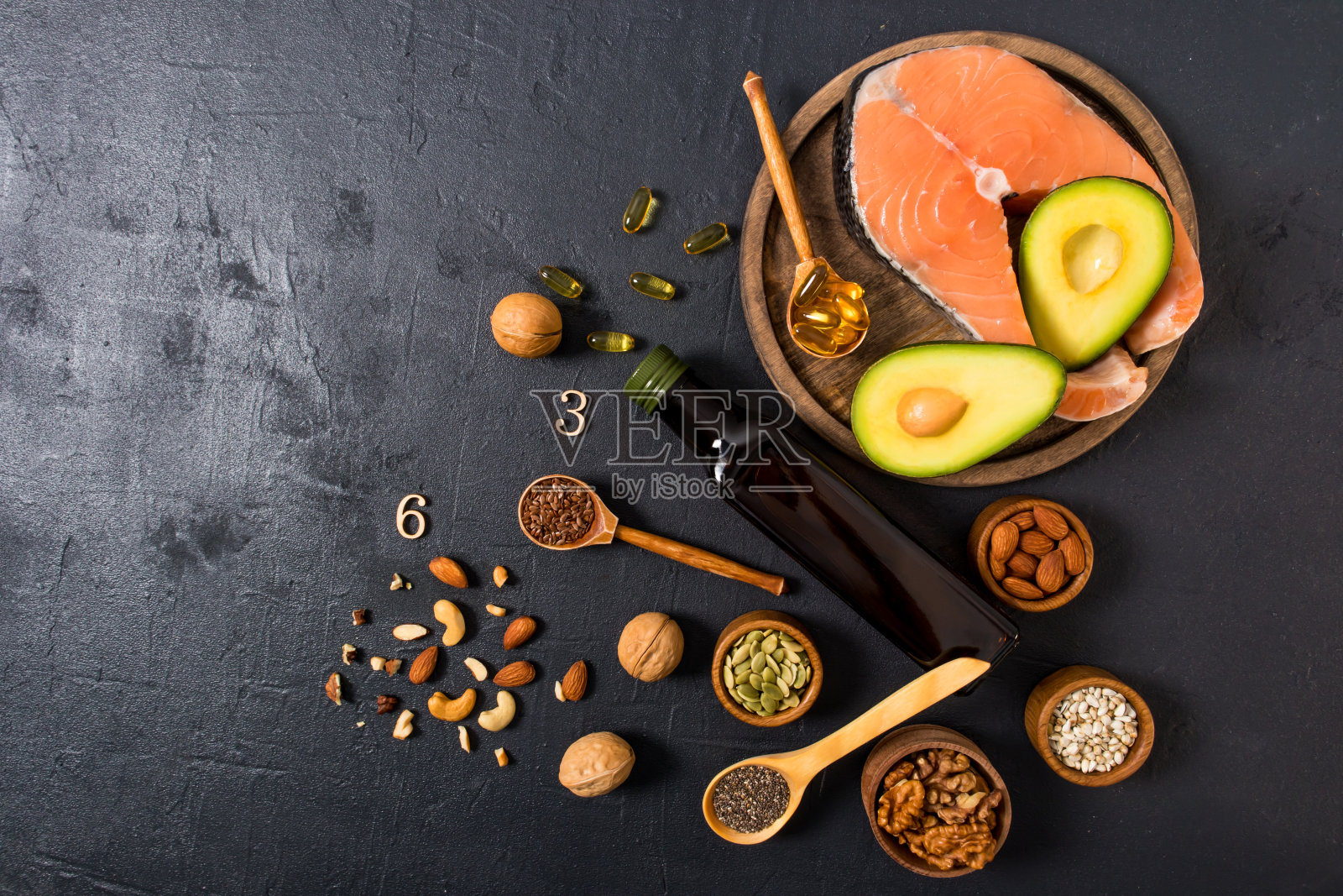 俯瞰一个圆形木制托盘与新鲜的鲑鱼牛排，一瓶亚麻仁油，坚果，种子，欧米加3胶囊。适当营养的概念。照片摄影图片