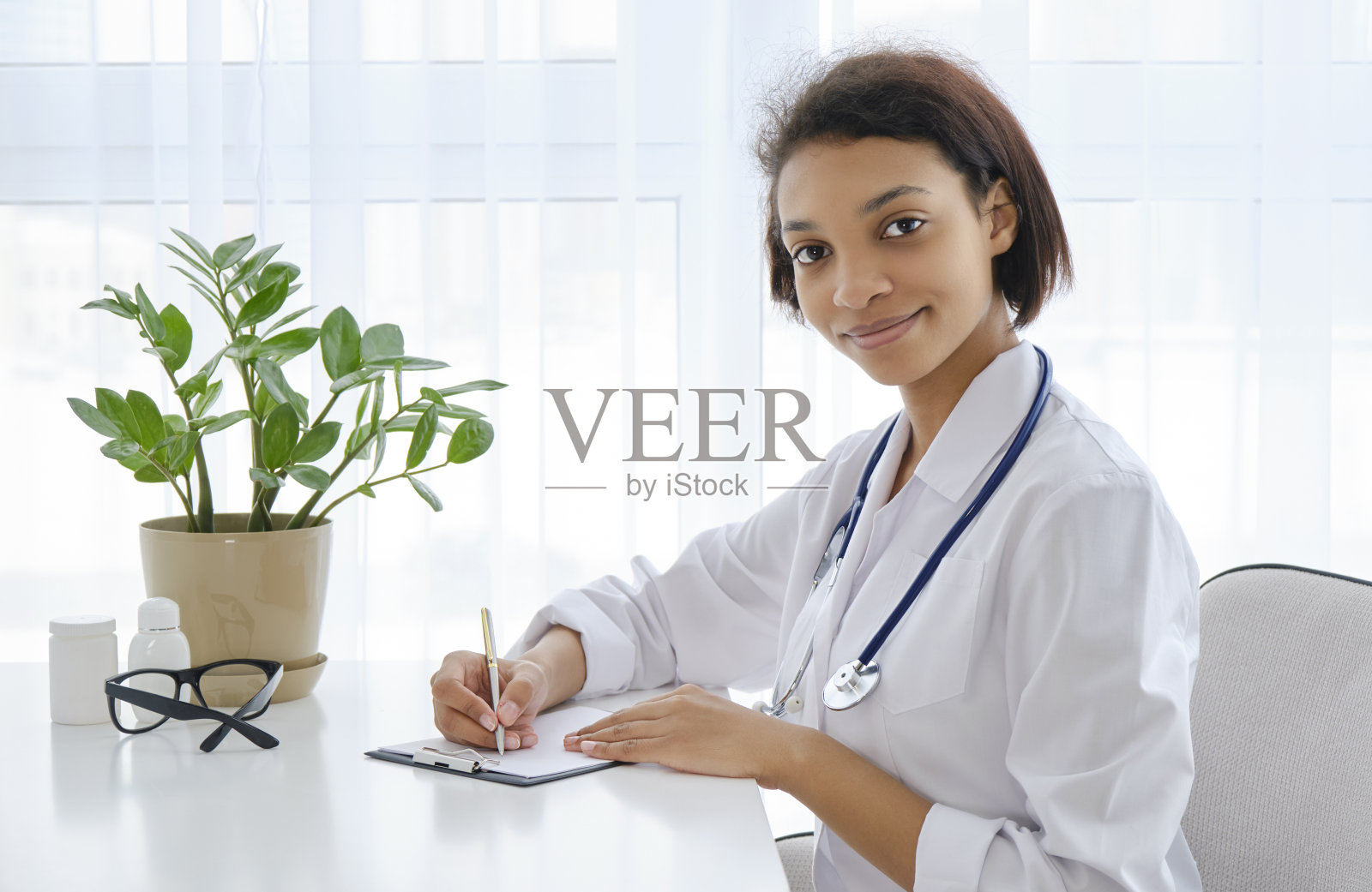 非裔美国人微笑的女医生坐在医疗办公室的桌子上，在电脑上工作照片摄影图片