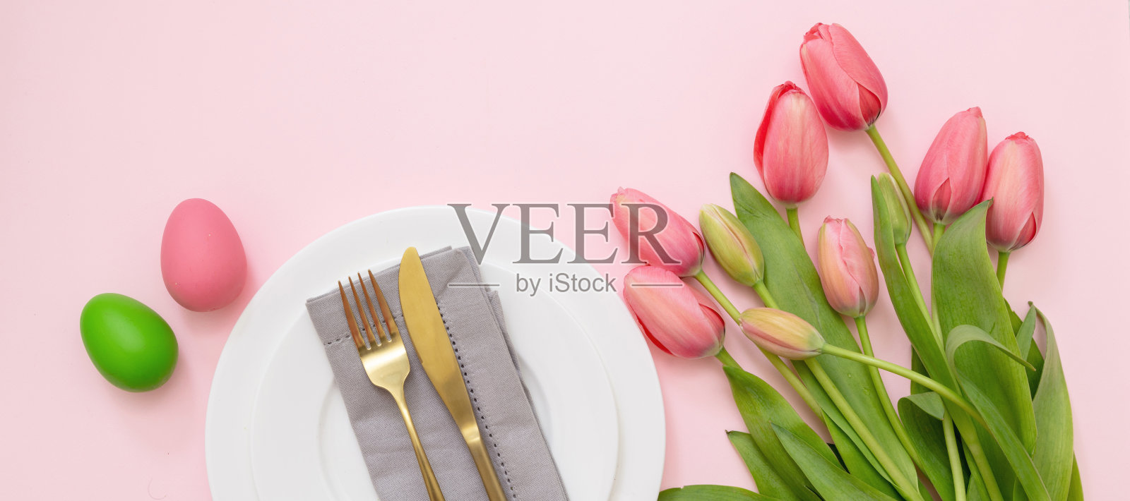 复活节表设置。鸡蛋和郁金香的柔和颜色和金色的餐具在粉红色，头顶照片摄影图片