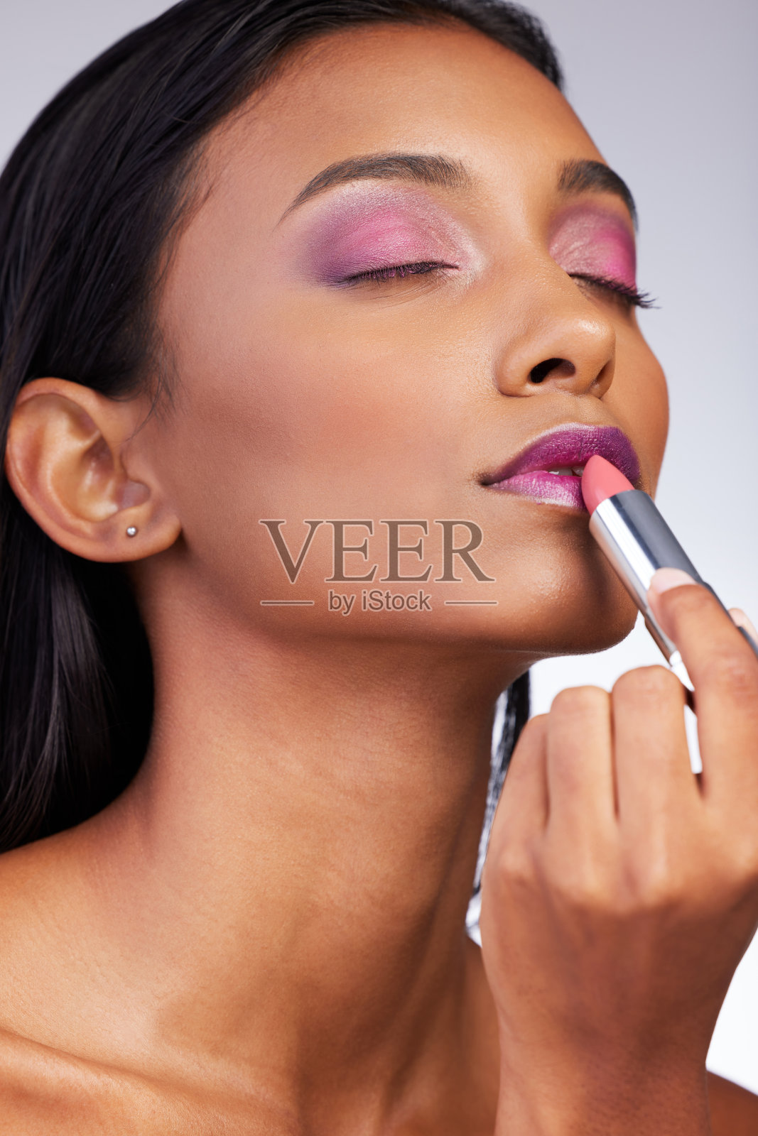 工作室拍摄的一个迷人的年轻女子，在灰色的背景上涂口红照片摄影图片