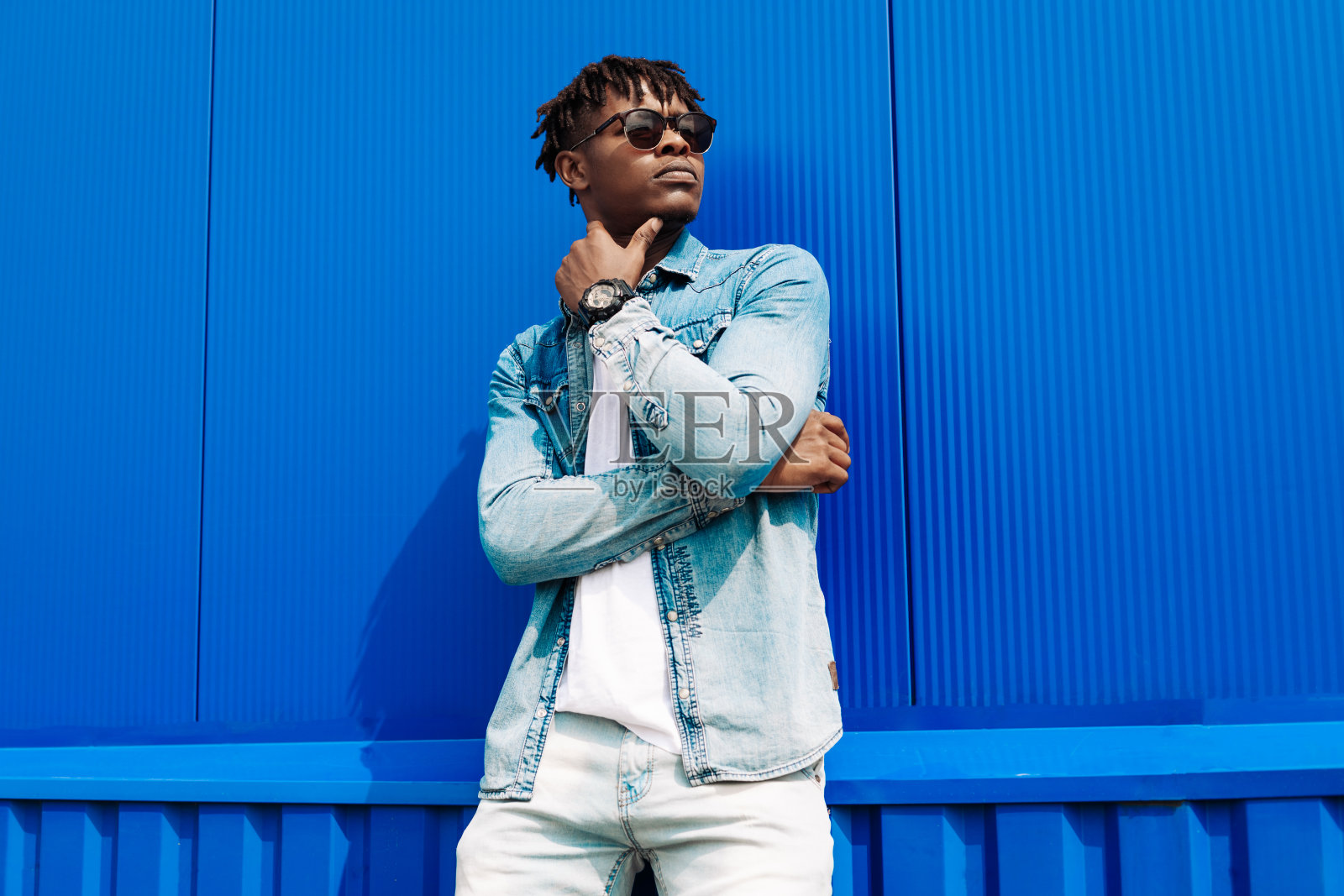 时尚肖像时尚深色皮肤的男人，穿着夹克和牛仔裤。时尚的男人靠在蓝色的墙上摆姿势照片摄影图片