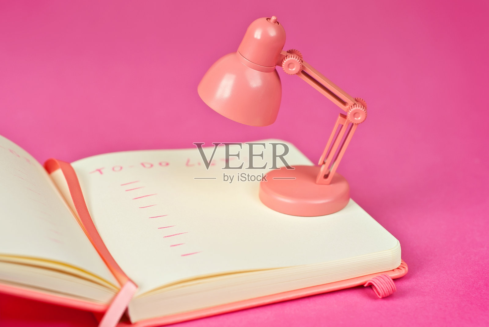 粉色背景的笔记本。笔记本旁边的玩具台灯。拷贝空间和笔记本中文字的自由空间。设计的模型。“待办事项清单”这个词是用铅笔写的。创造力的概念。照片摄影图片