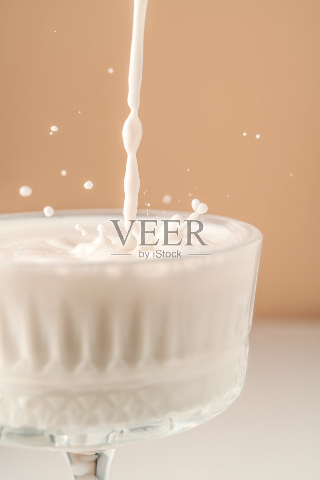 牛奶倒入一个漂亮的水晶玻璃杯，溅得到处都是。照片摄影图片
