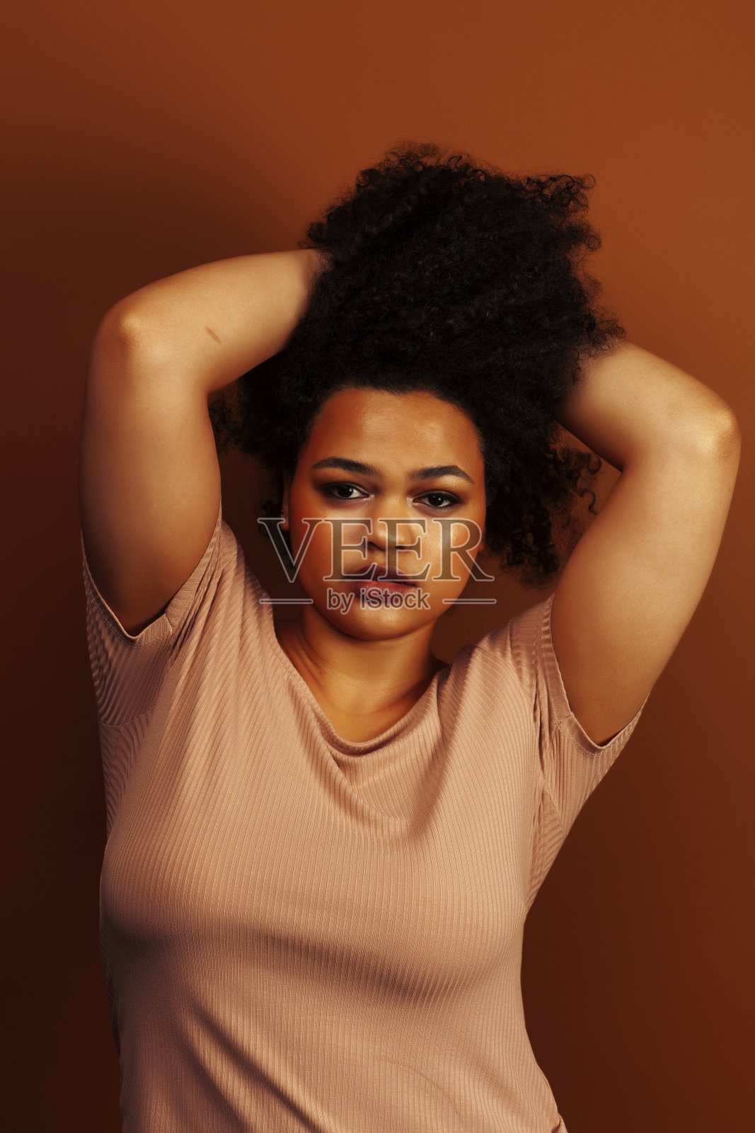 漂亮的年轻非洲裔美国妇女与卷曲的头发摆愉快的手势在棕色的背景，生活方式的人的概念照片摄影图片