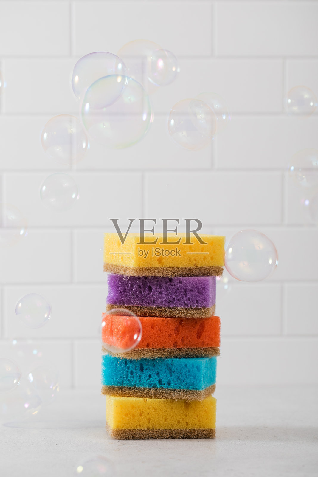 五颜六色的洗碗海绵堆在一起，肥皂泡四处飞舞。洗碗的概念照片摄影图片