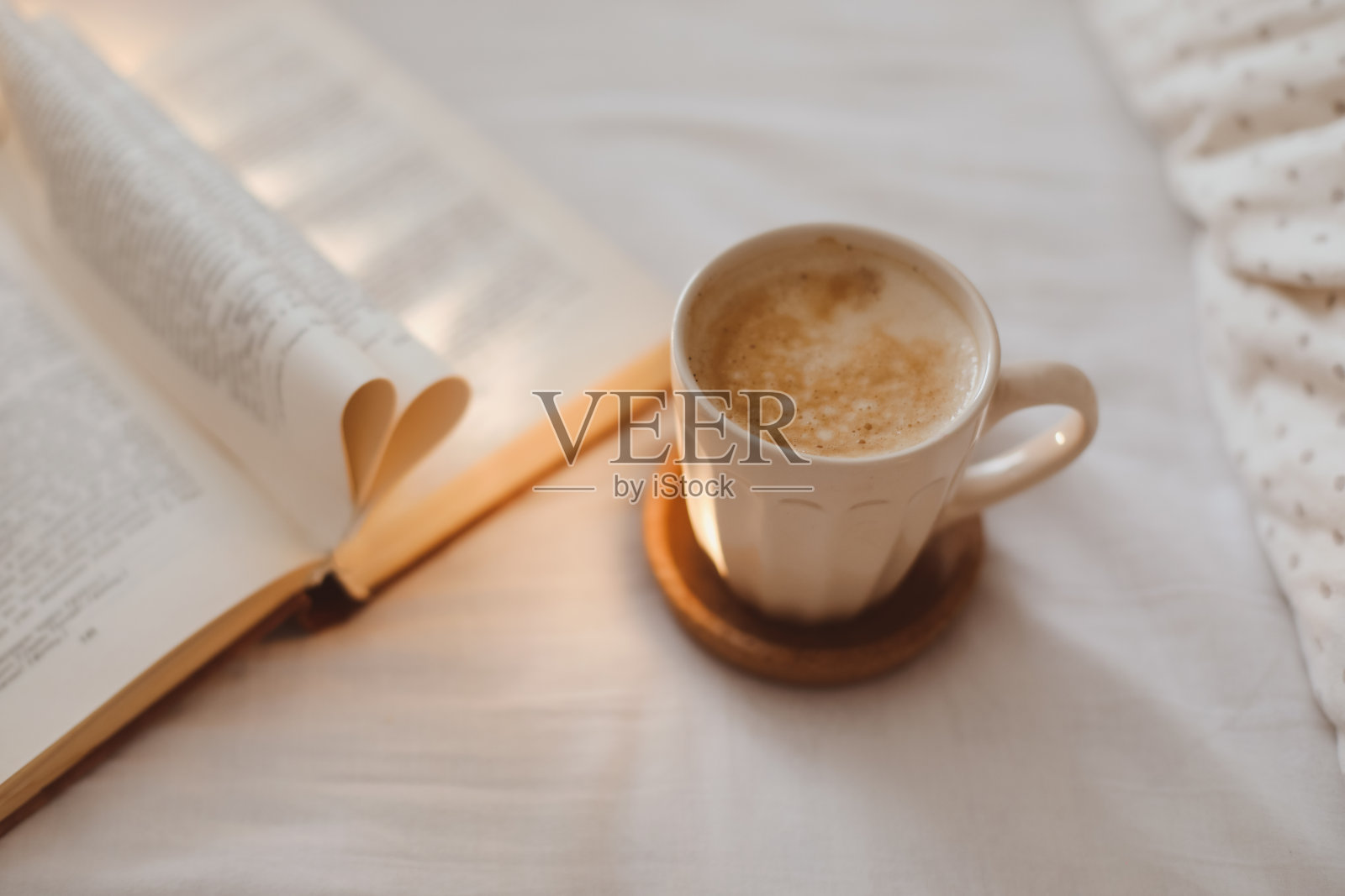 舒适的晨间作文，一个咖啡杯和一本折叠成心形的书躺在床上照片摄影图片