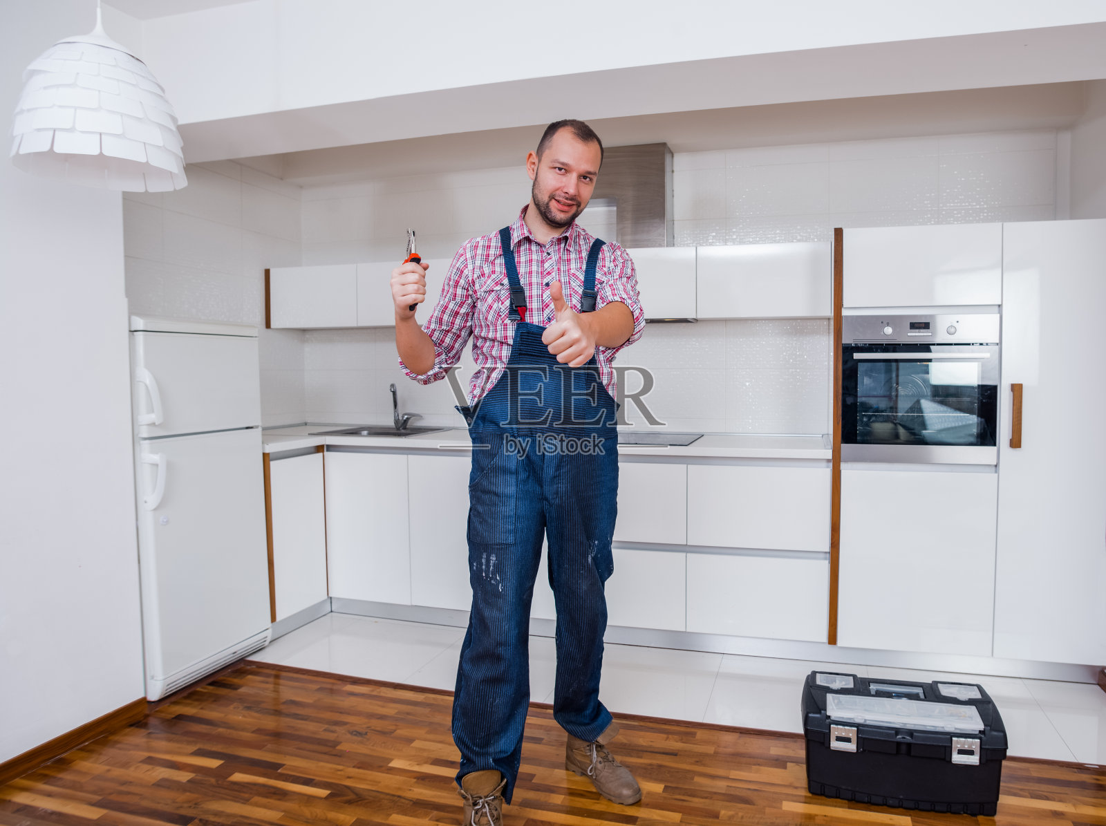 穿着制服的英俊工人站在厨房里的工具箱旁边照片摄影图片