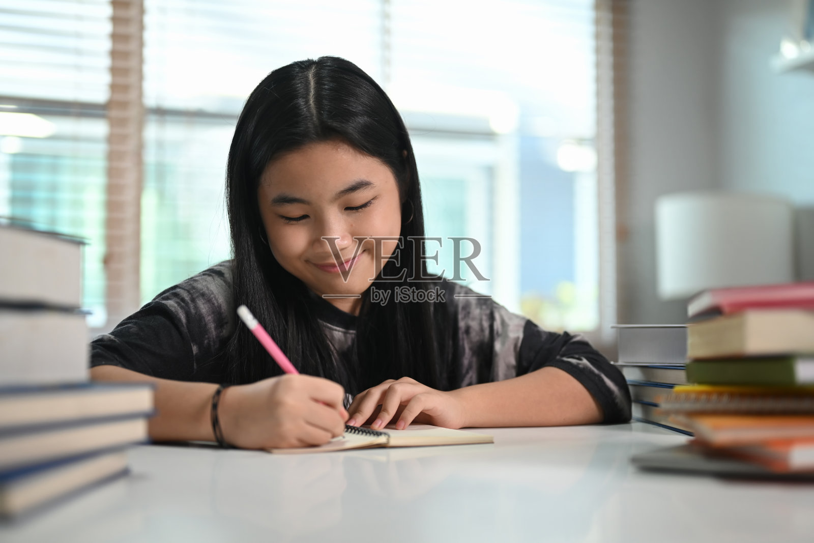 微笑的少女在家里做作业。照片摄影图片
