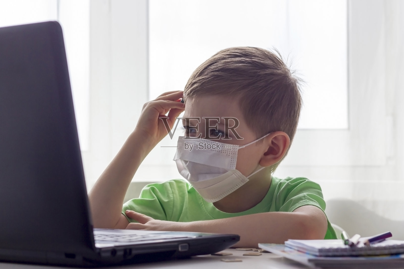 远程教育，在线教育。保持社会距离，隔离期间自我隔离。学龄前儿童或学童戴着医用口罩在家里用笔记本电脑学习，为发展学校做作业照片摄影图片