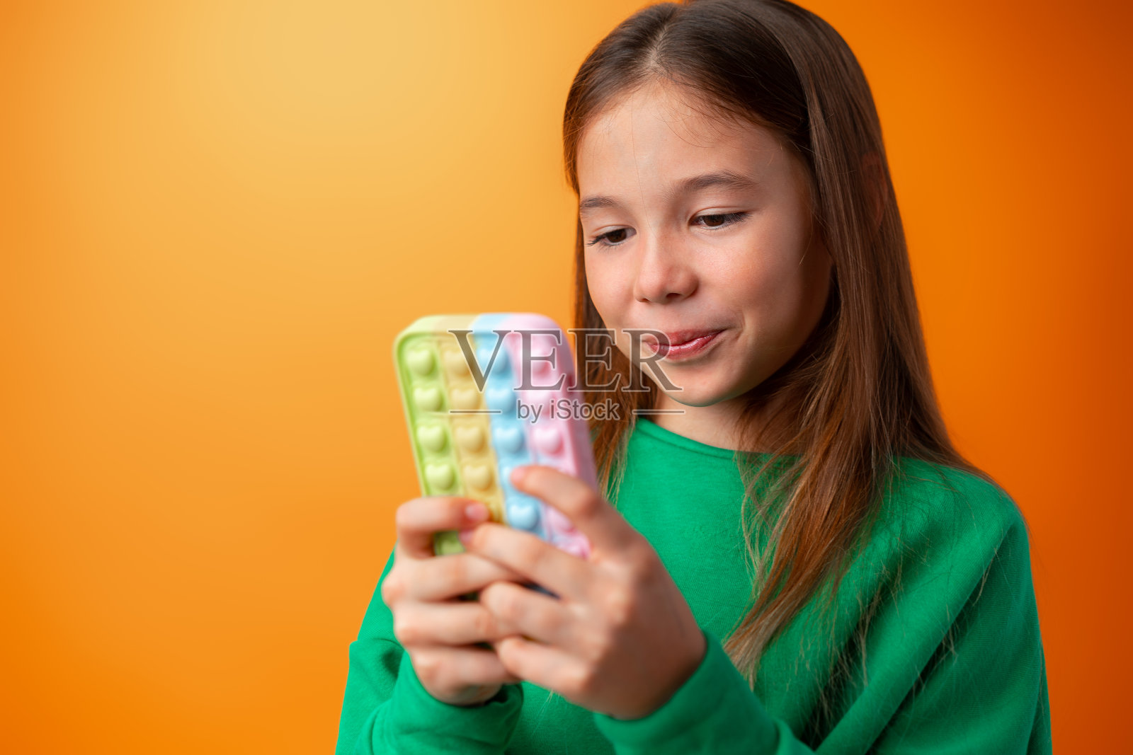 橘色背景下使用手机的可爱少女，面露喜色照片摄影图片