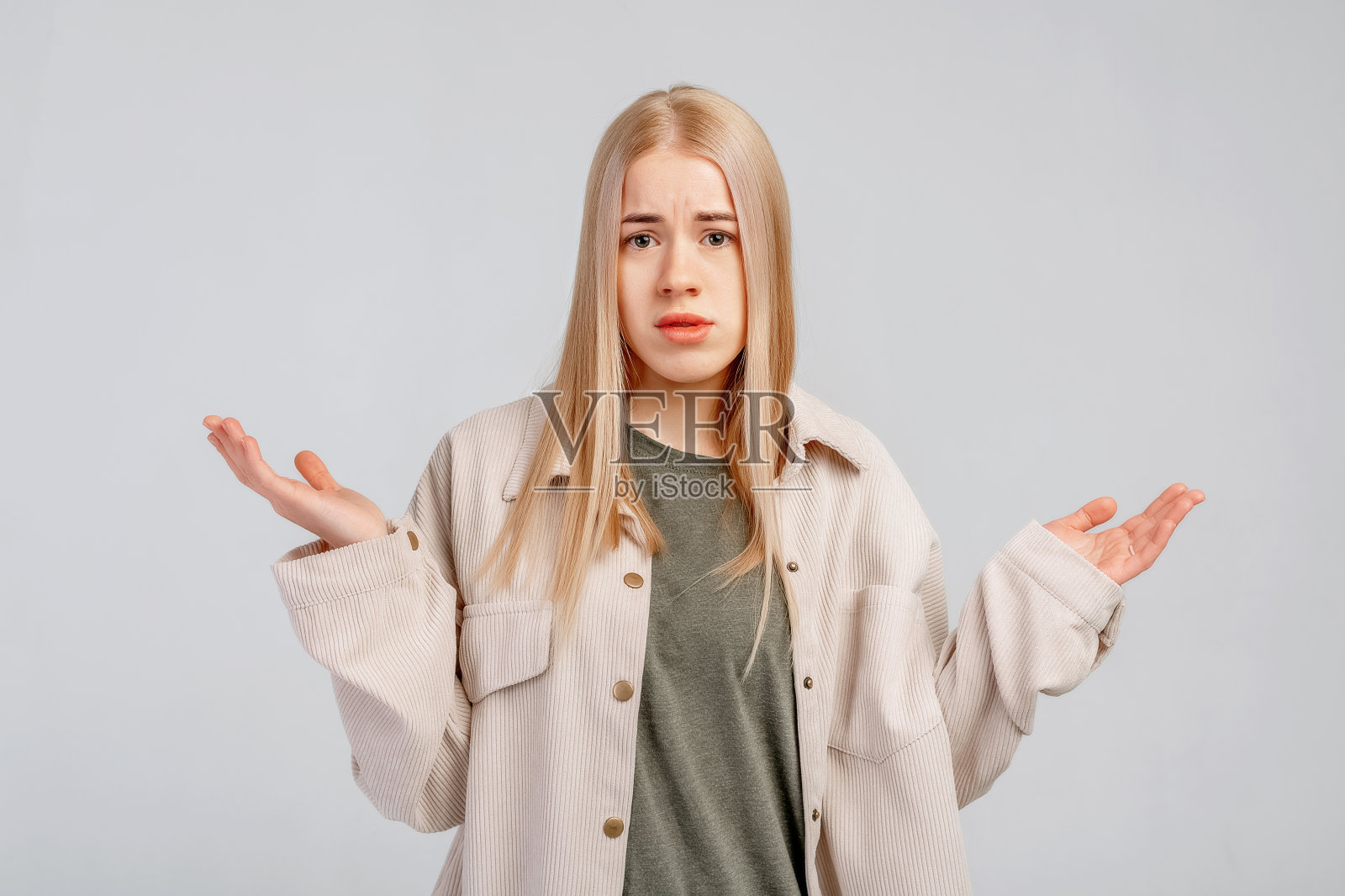 困惑的金发女孩看起来困惑和烦恼，不能理解什么奇怪的东西，摊开手，站在灰色的背景照片摄影图片