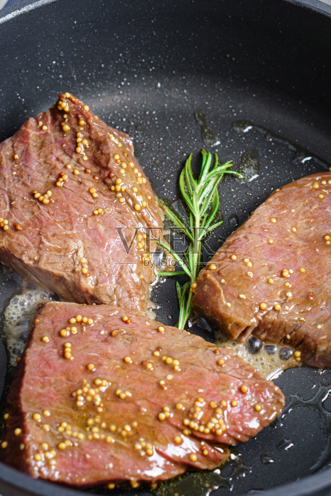 用迷迭香和芥菜籽在煎锅里烤牛排照片摄影图片