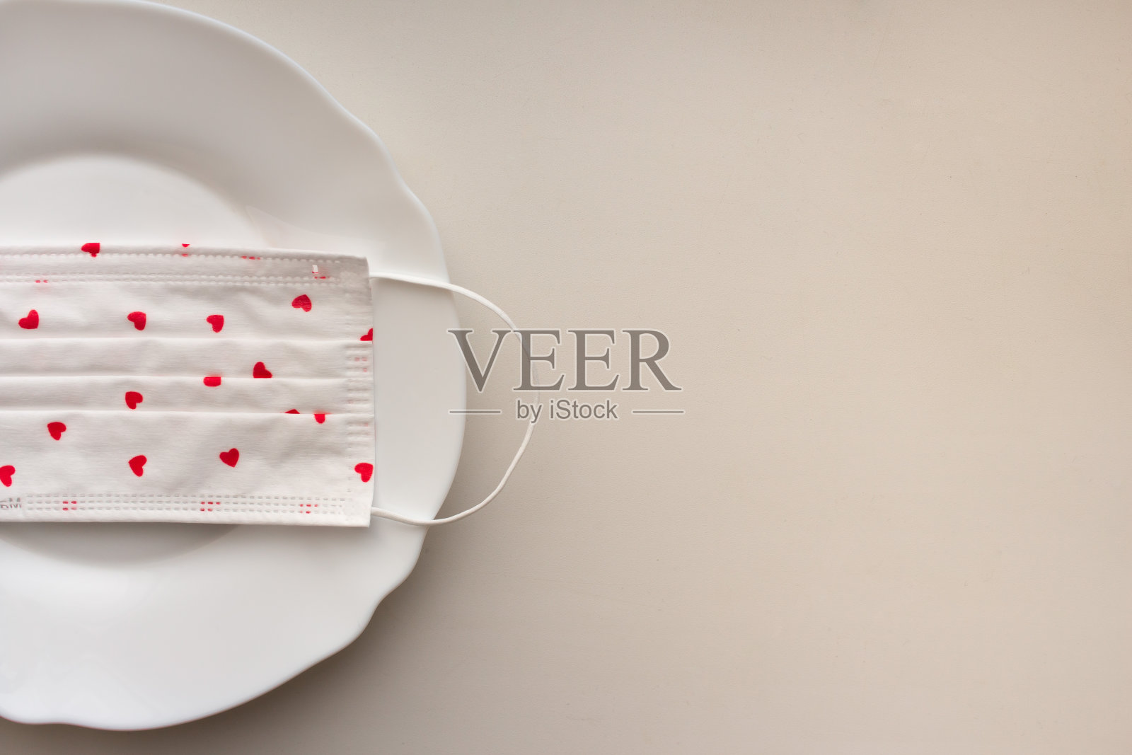 大流行和隔离期间的情人节。医用白色口罩与红心的图像在一个白色的干净盘子上的白色背景，俯视图。餐厅在家里。假期安全。浪漫的晚餐检疫照片摄影图片