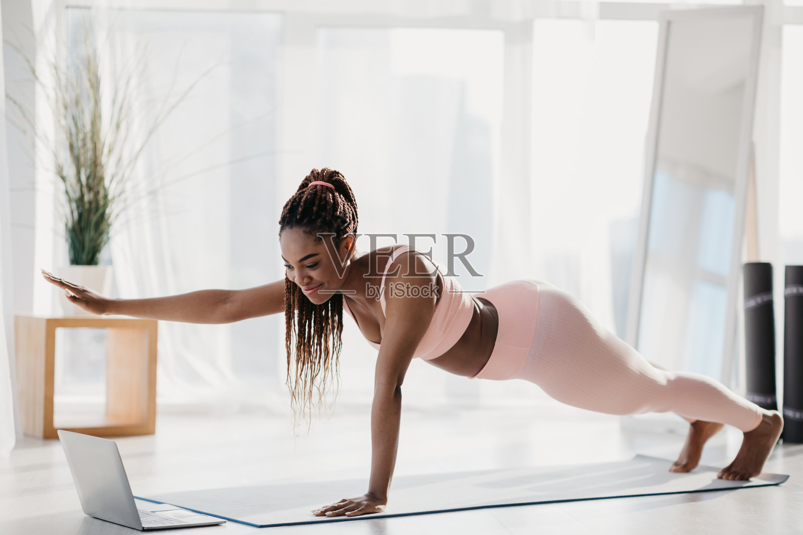身材匀称的年轻黑人女子，伸开手臂站在平板上，在家里用笔记本电脑学习在线视频教程照片摄影图片