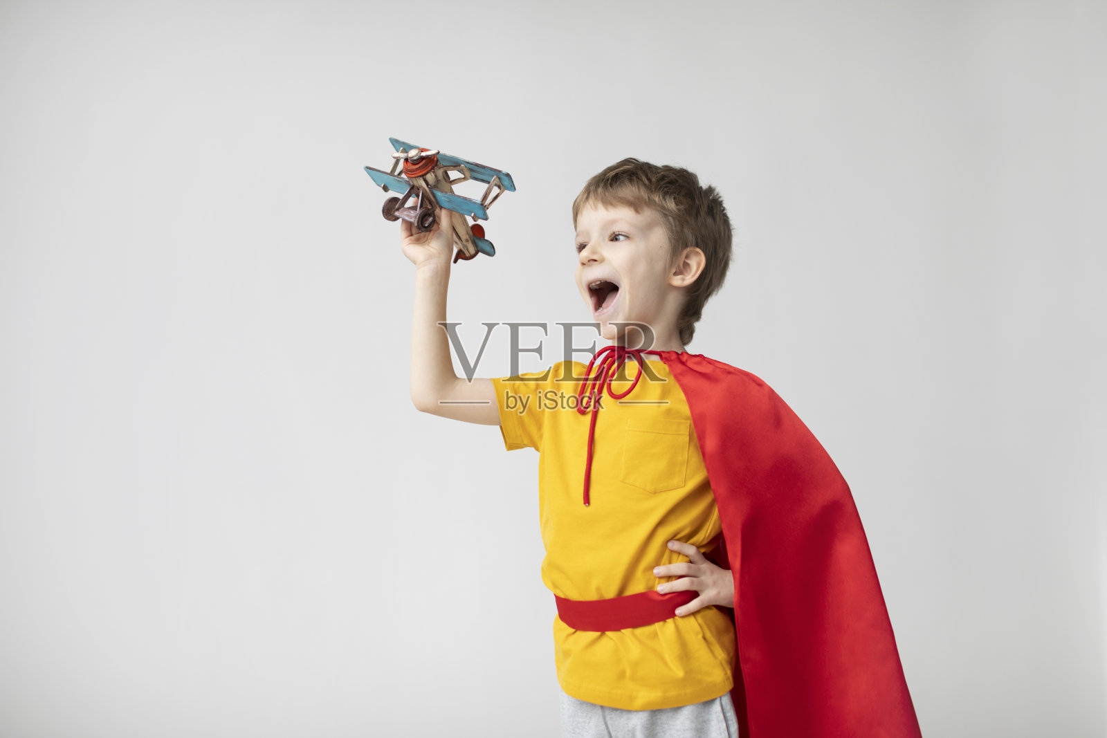 身着红色斗篷的梦幻男孩在玩飞机玩具。照片摄影图片