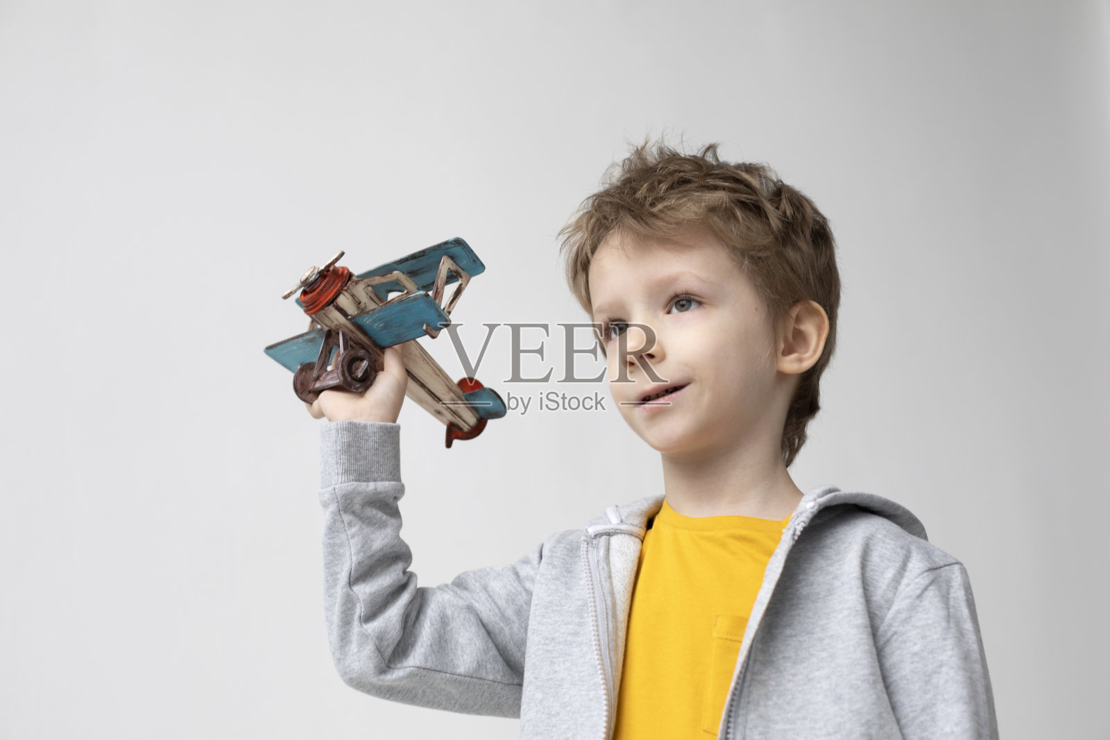 在白色的背景下，一个手拿木飞机、面带微笑的可爱男孩正在做梦。幸福和自由照片摄影图片