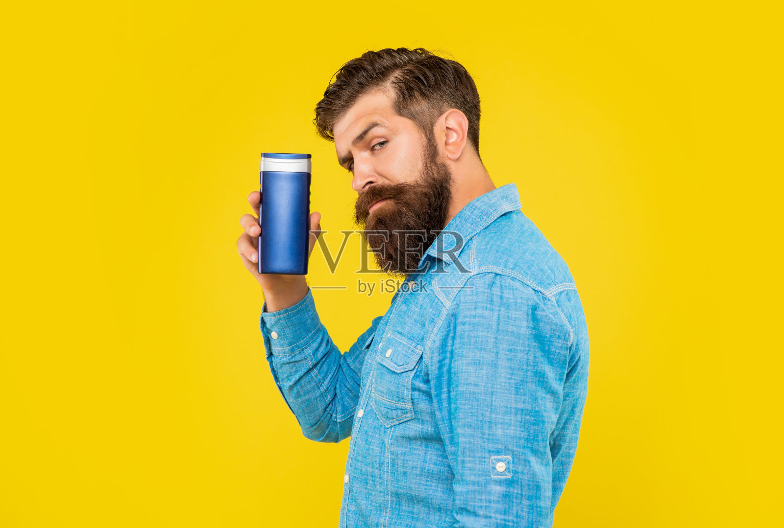 成熟野蛮的大胡子男人拿着香波瓶对着黄色背景进行护肤照片摄影图片