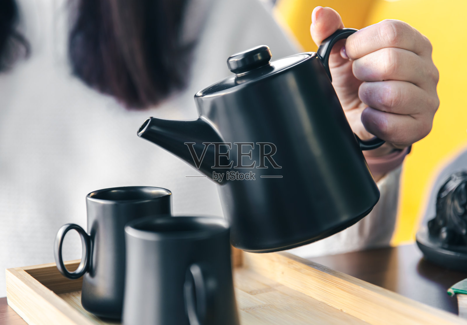 特写镜头，一名妇女将茶从黑色茶壶倒入黑色茶杯中。照片摄影图片