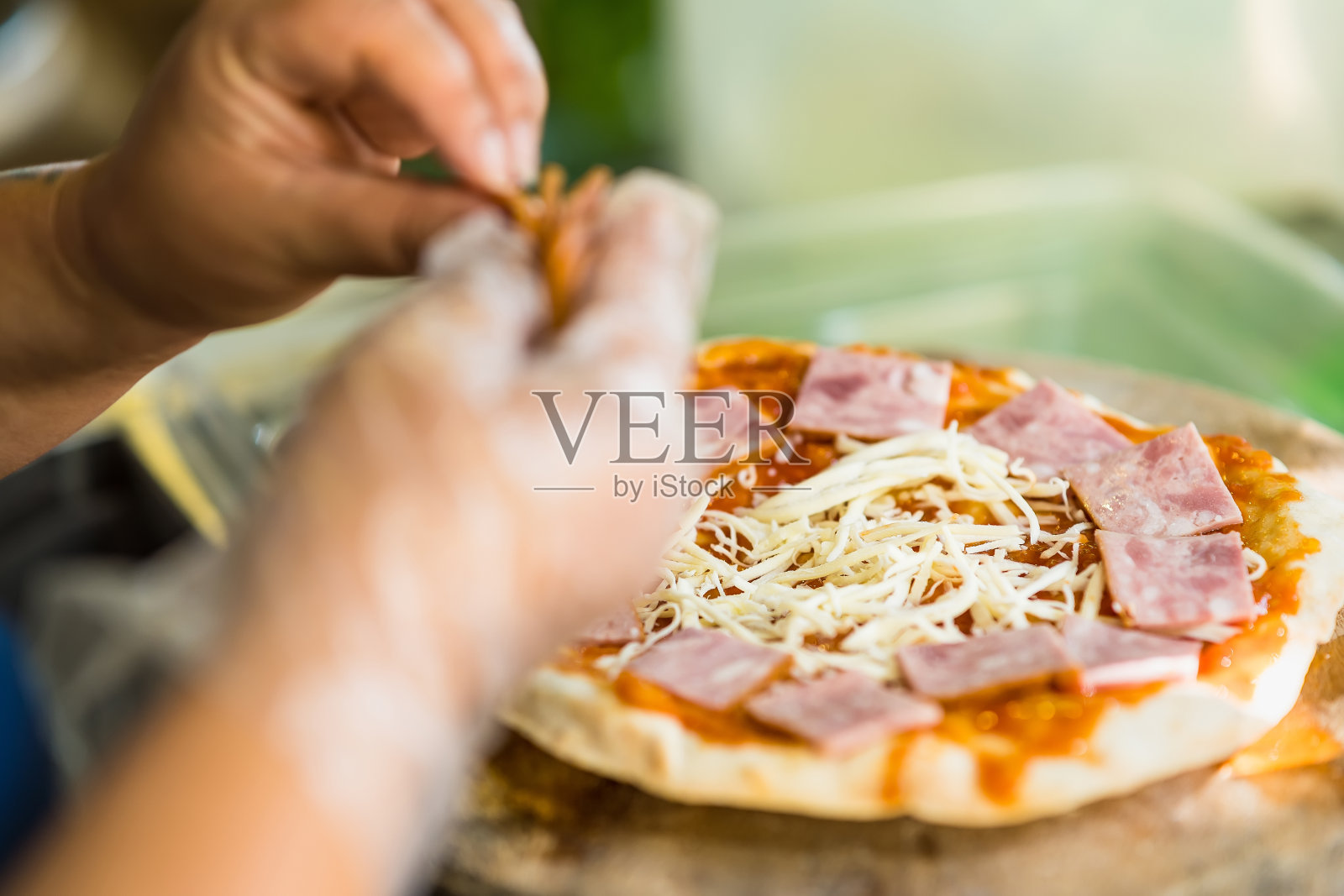厨师正在用火腿准备披萨，然后把它放进烤箱。使用传统的柴火照片摄影图片