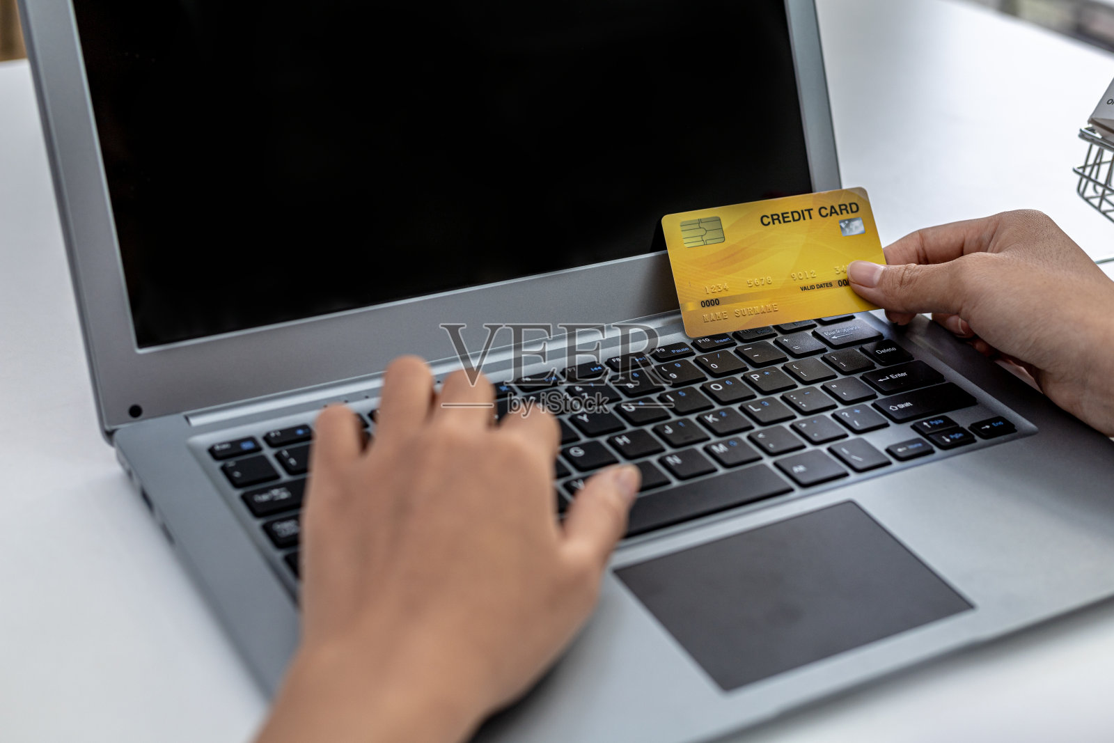 女人拿着信用卡在笔记本电脑键盘上打字，她正在填写信用卡信息，以支付互联网购物网站上的订单。网上购物和信用卡支付概念照片摄影图片