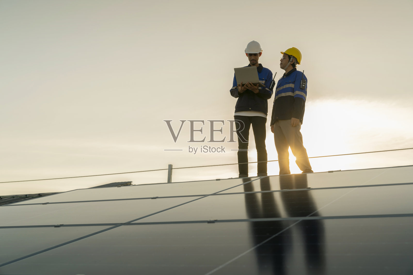 专业技术员专业工程师带着笔记本电脑和平板电脑进行维护检查，在阳光下安装工厂屋顶太阳能电池板。工程师小组调查检查太阳能电池板屋顶。照片摄影图片