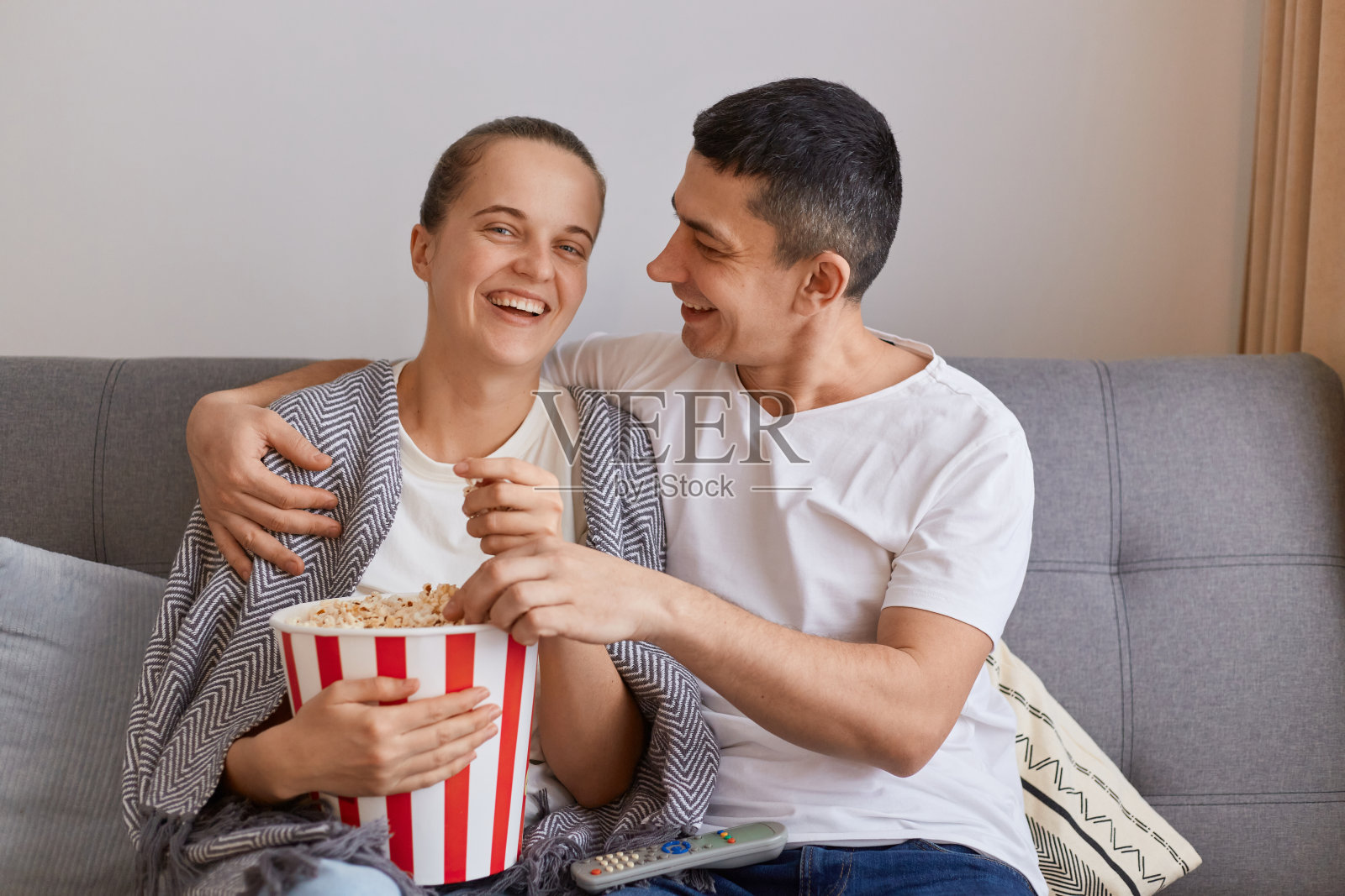 幸福积极的一家人坐在沙发上看搞笑电影或喜剧电影，一起度过休闲时光，穿着休闲的衣服，丈夫用爱和温柔的眼神看着妻子。照片摄影图片