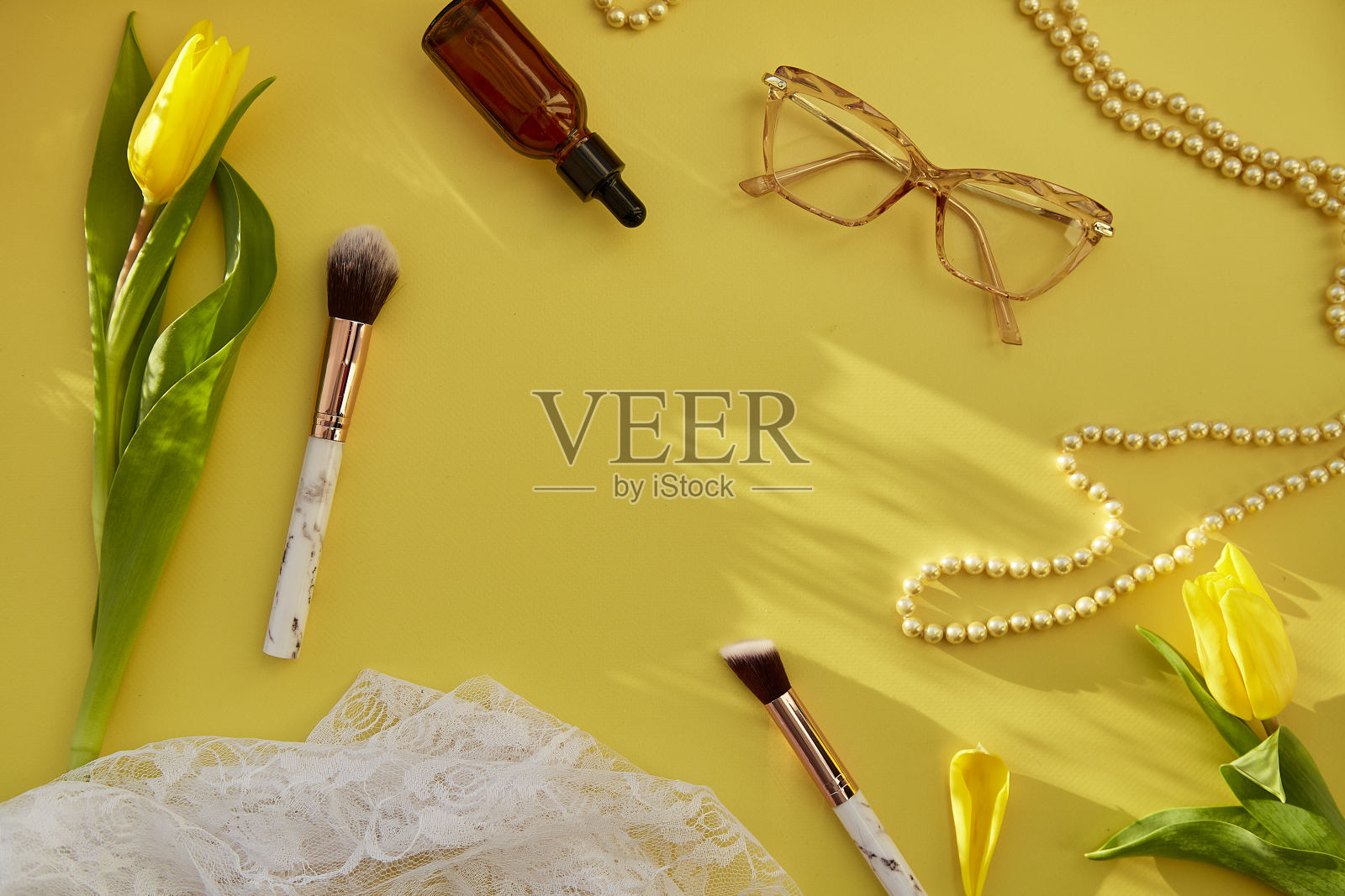 女性平躺着珍珠，化妆刷，眼镜，血清滴管和花边。黄色的郁金香带着时尚的阴影。美容卡的概念。本空间照片摄影图片