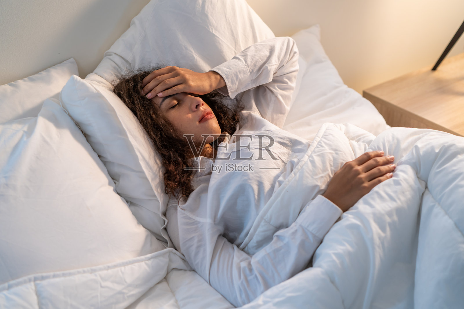 拉丁美人躺在床上卧室在黑暗的夜房。有吸引力的年轻女性在睡衣睡在舒适的枕头感觉头痛和呕吐，而睡在家里。照片摄影图片