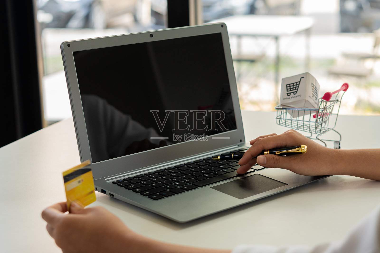 年轻女子手持信用卡，使用笔记本电脑工作电子商务网上银行消费货币网上产品购买，通过信用卡注册在网上购物。照片摄影图片