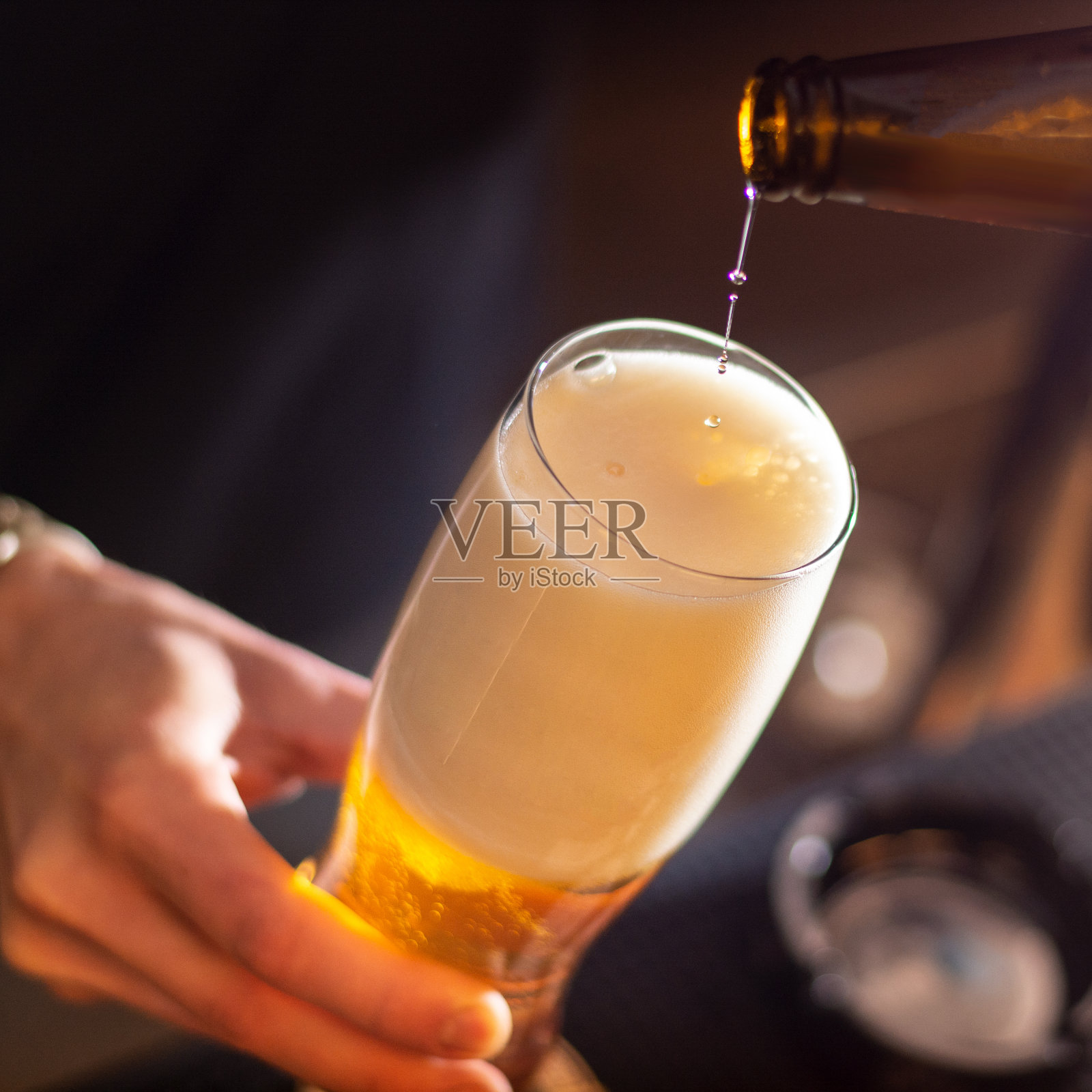 酒吧里，酒保把精酿啤酒倒进玻璃杯里照片摄影图片