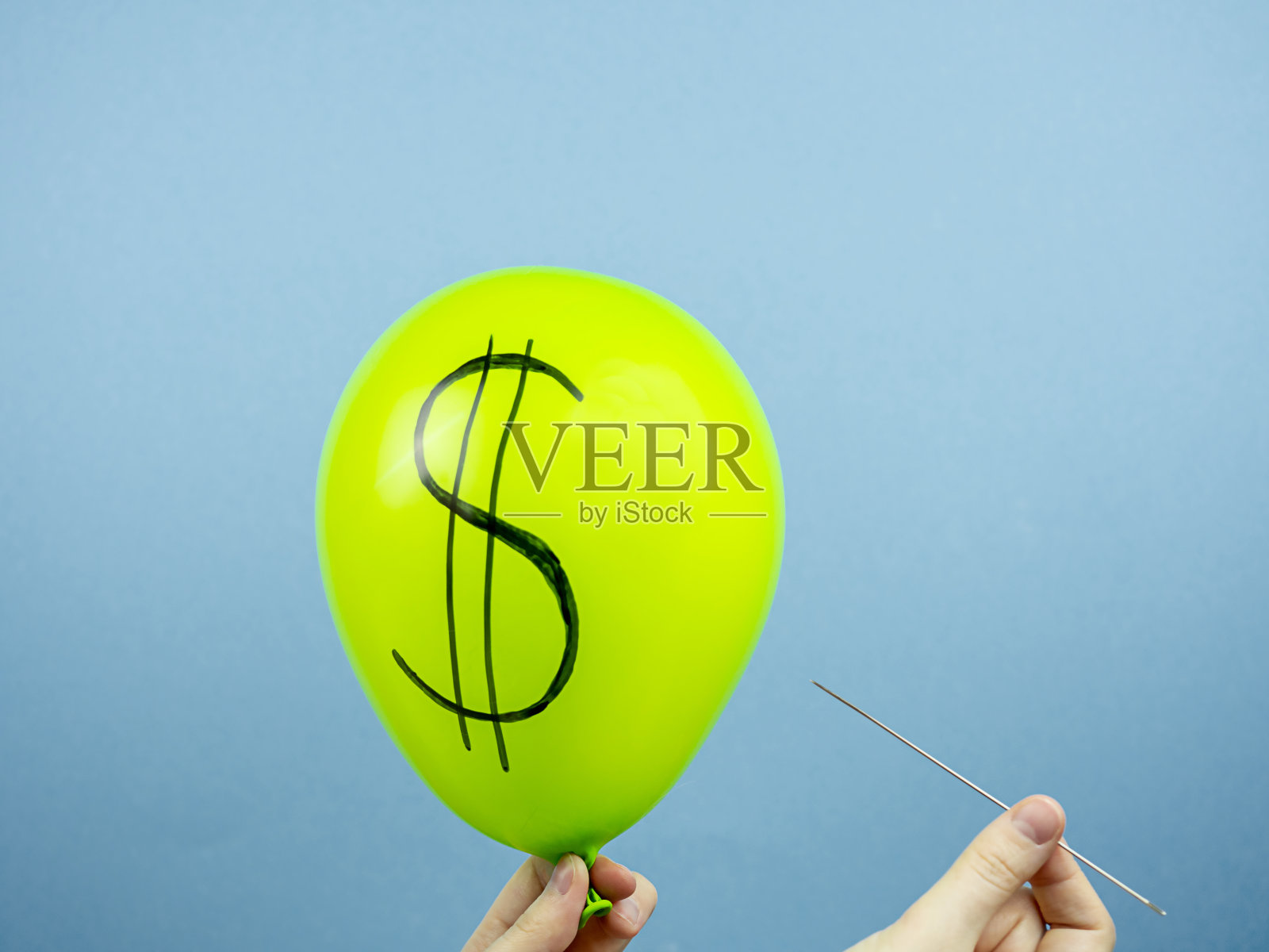 绿色的球，上面有美元的符号，手上有一根针，背景是蓝色的。货币概念，货币汇率照片摄影图片
