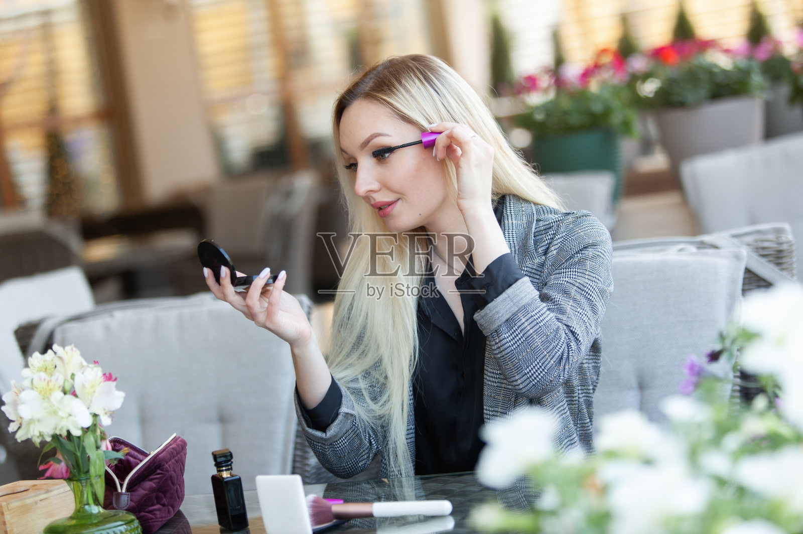 年轻迷人的金发美女在咖啡馆的夏季露台上化妆(用睫毛膏刷涂她的睫毛)照片摄影图片